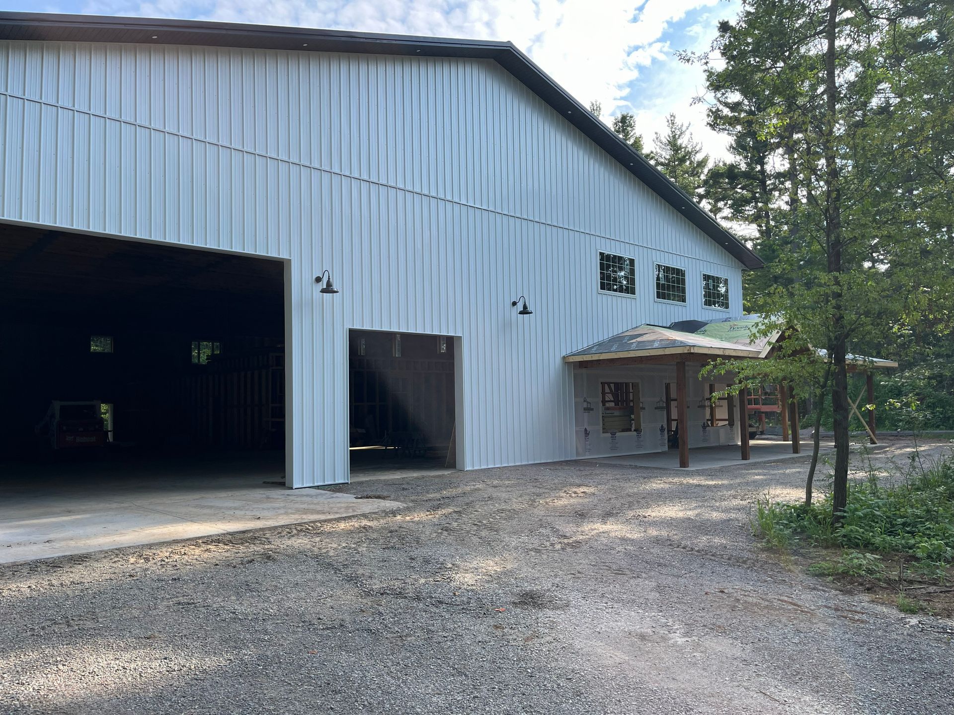 White metal barn with large open doors, gravel driveway, and a small covered entrance.