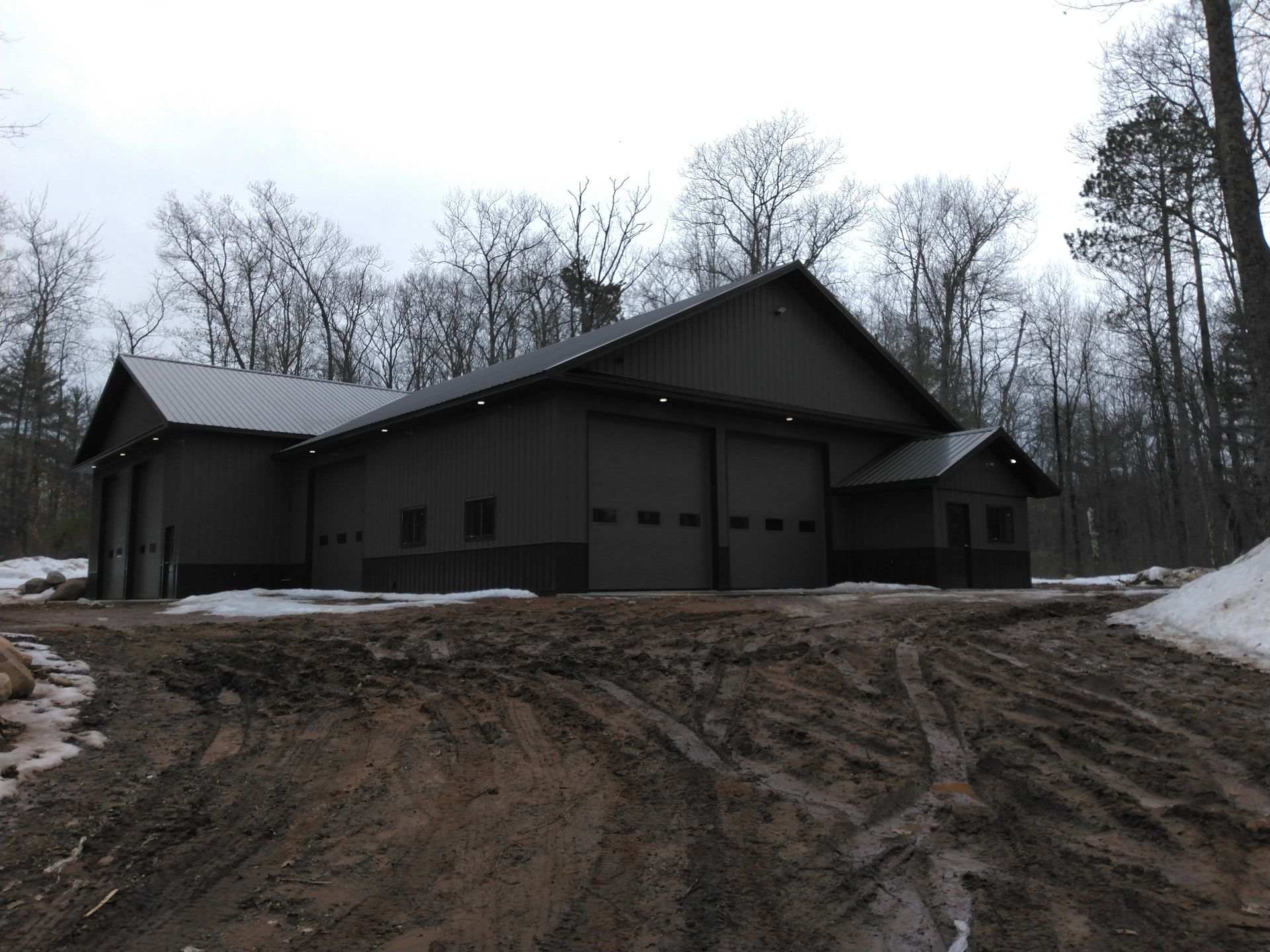 Dark brown building with garage doors, in a muddy setting with trees.