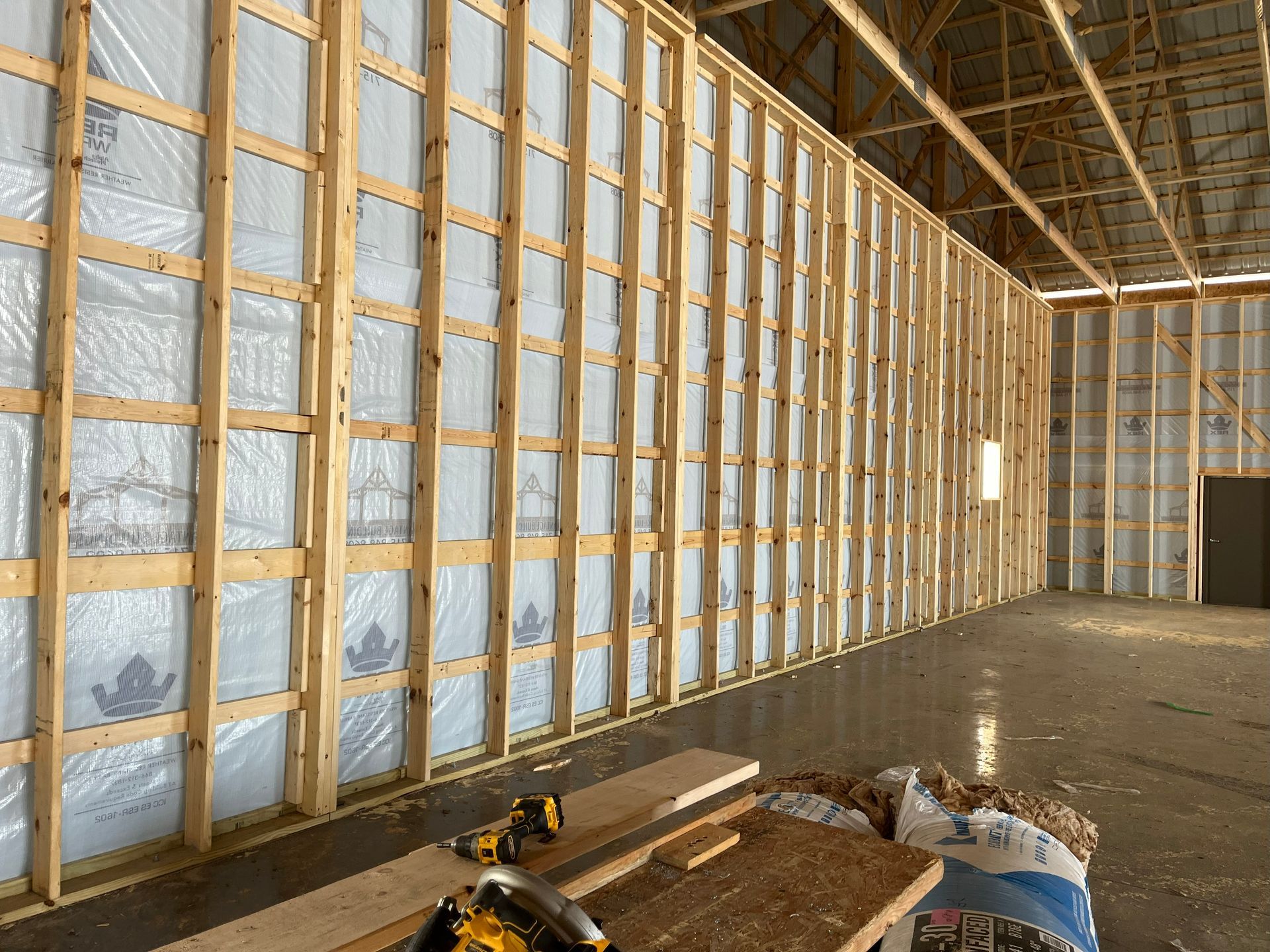 Interior view of a building under construction, showing wooden framing with insulation between the studs.