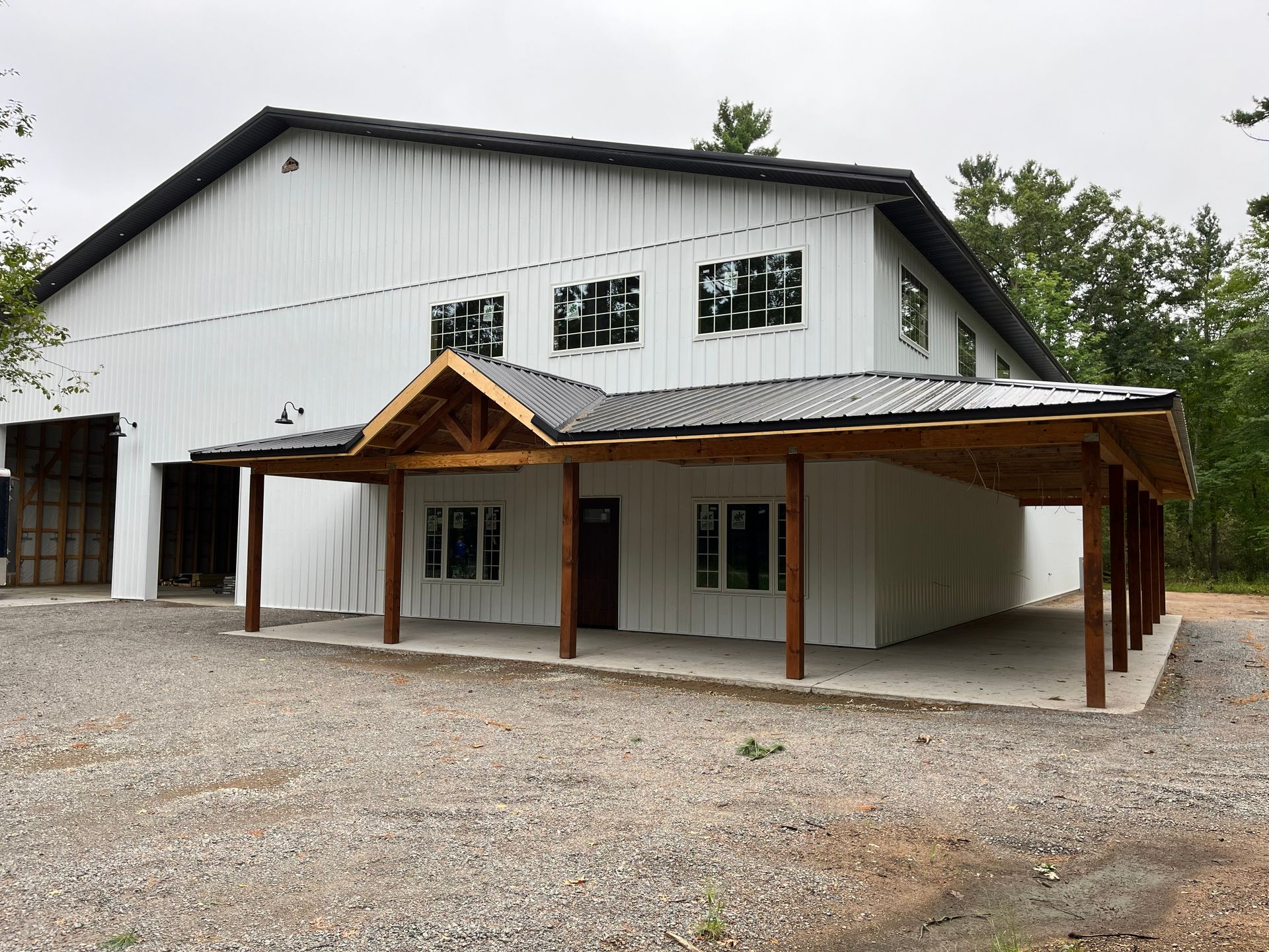 White two-story building with a porch. Dark roof, gravel yard, and wooden posts supporting the covered porch.