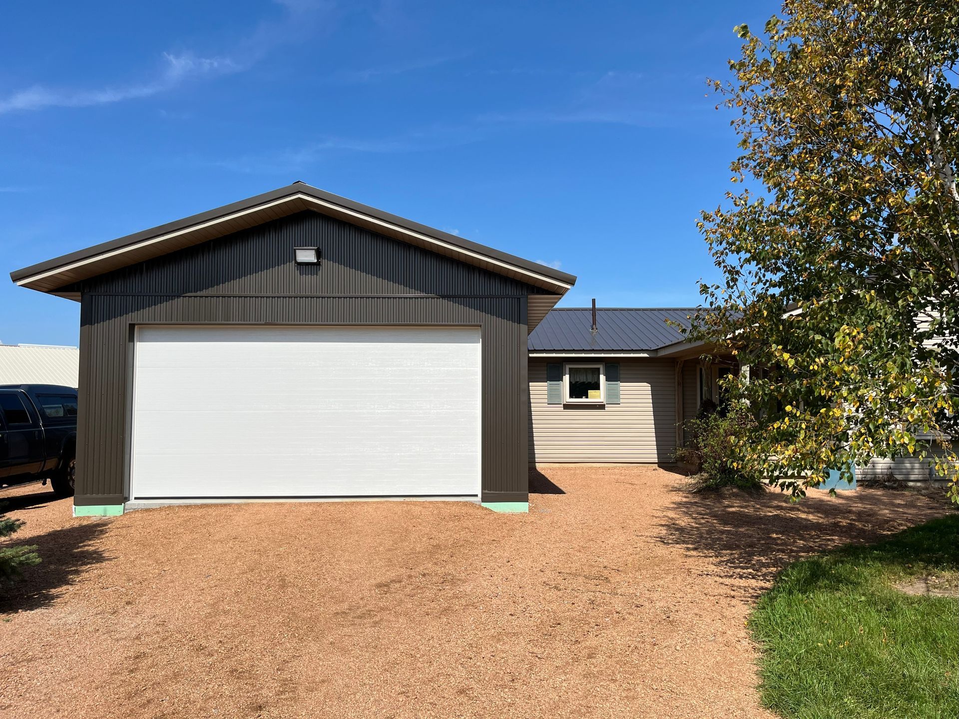 Brown garage with white door and adjacent house with a blue sky background.