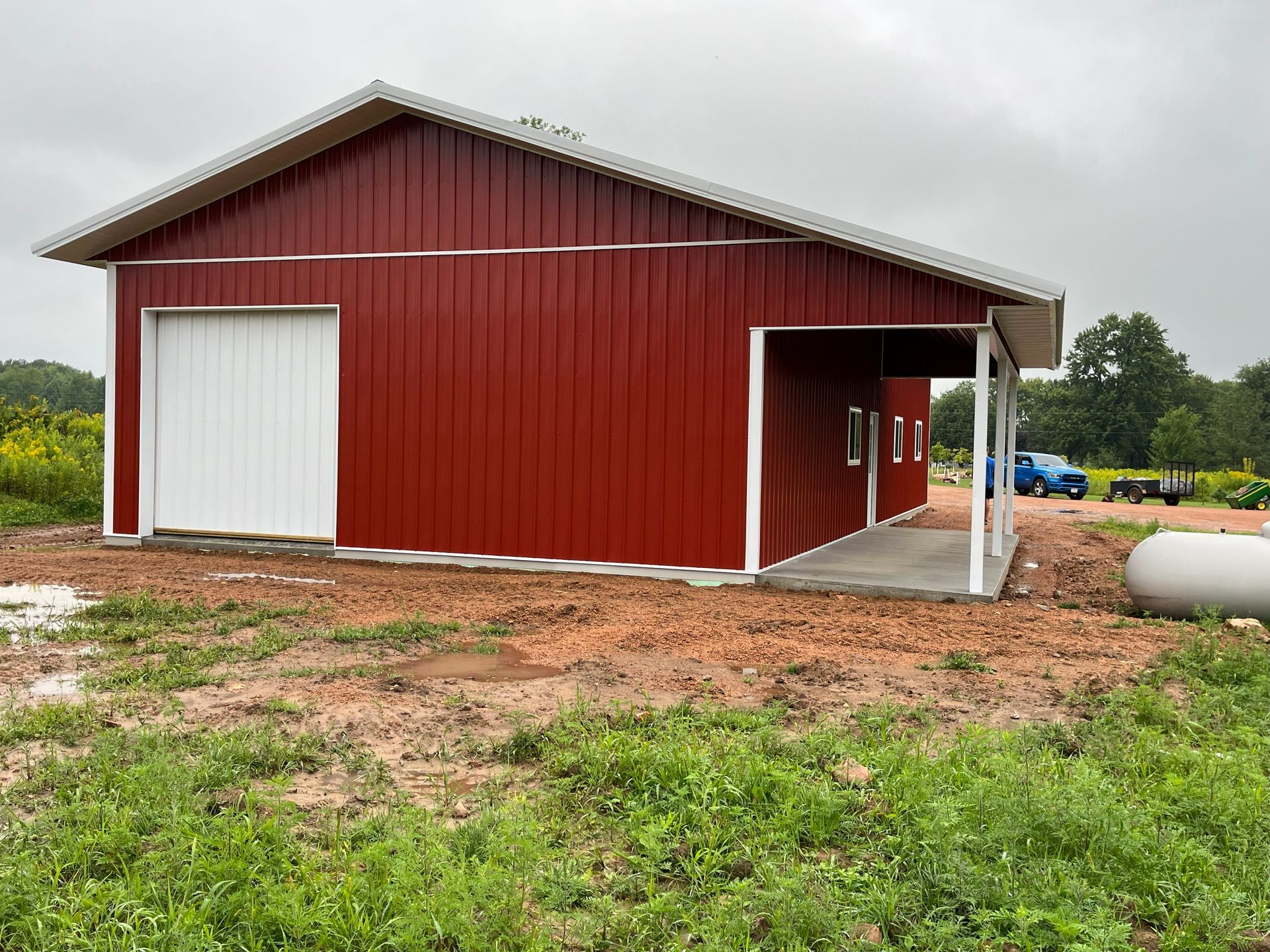 Red metal barn with white trim, garage door, and covered porch on a cloudy day.