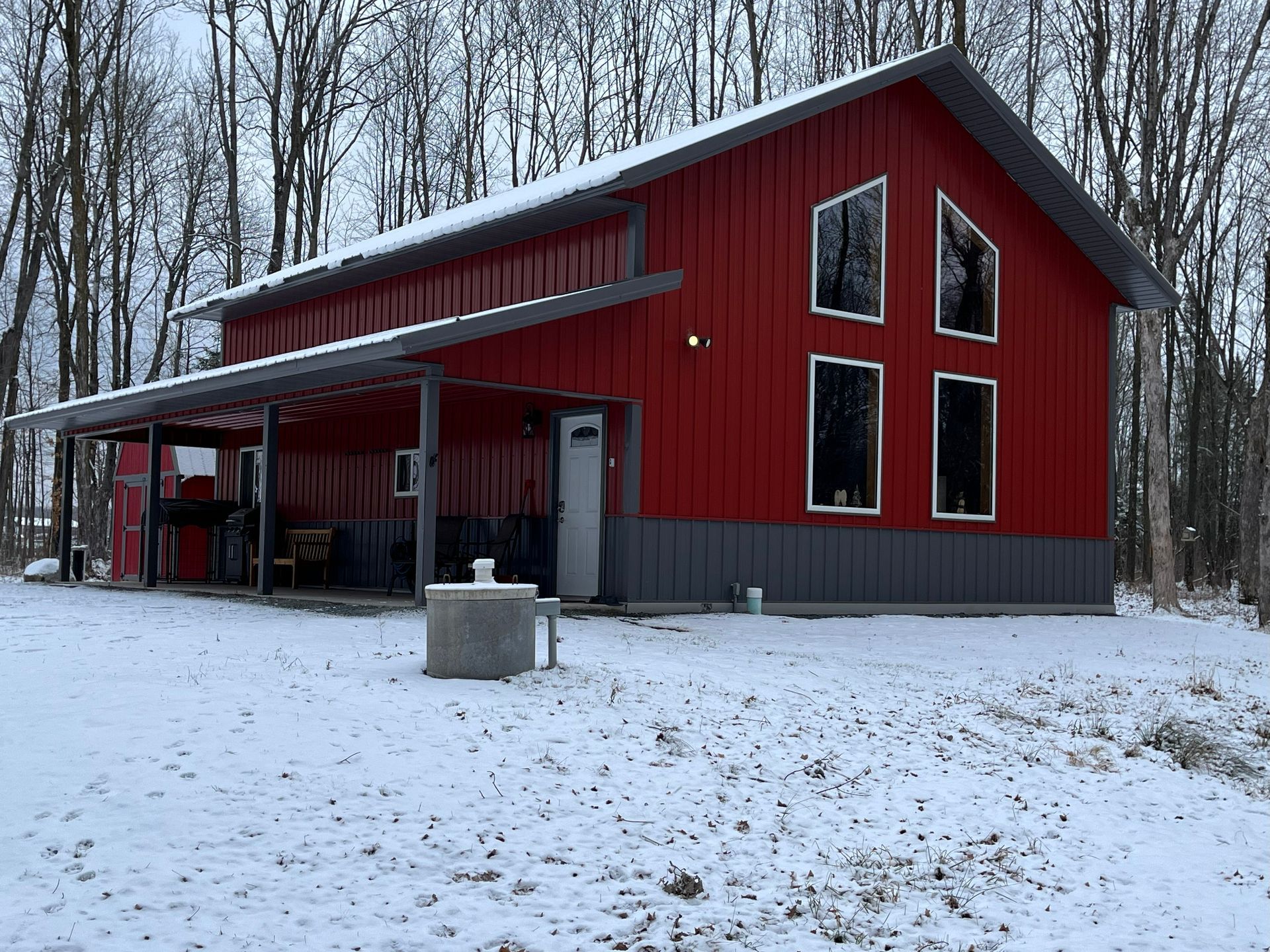 Red barn-style building with a gray awning and trim in a snowy forest.