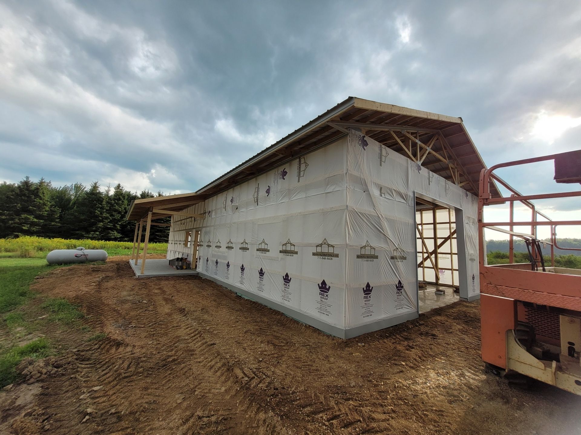 Construction of a building; wood frame with sheathing, tar paper, and a partial roof. Outdoors, cloudy sky.