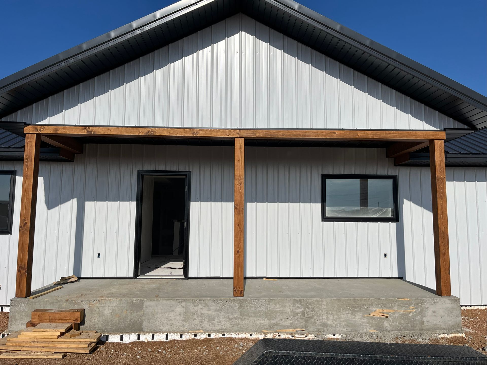 White house with brown wooden porch under a blue sky. Concrete patio.