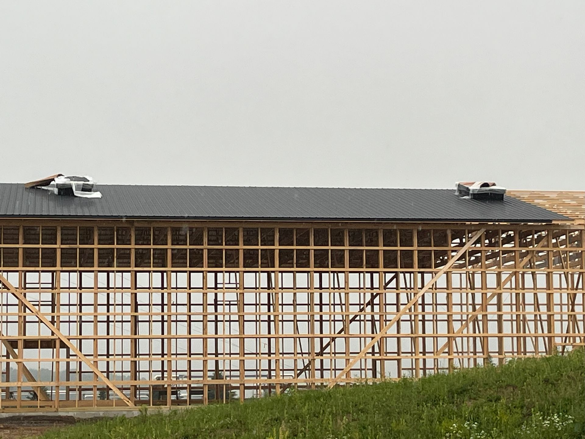 Wooden building frame with a partially completed black roof, vents visible.