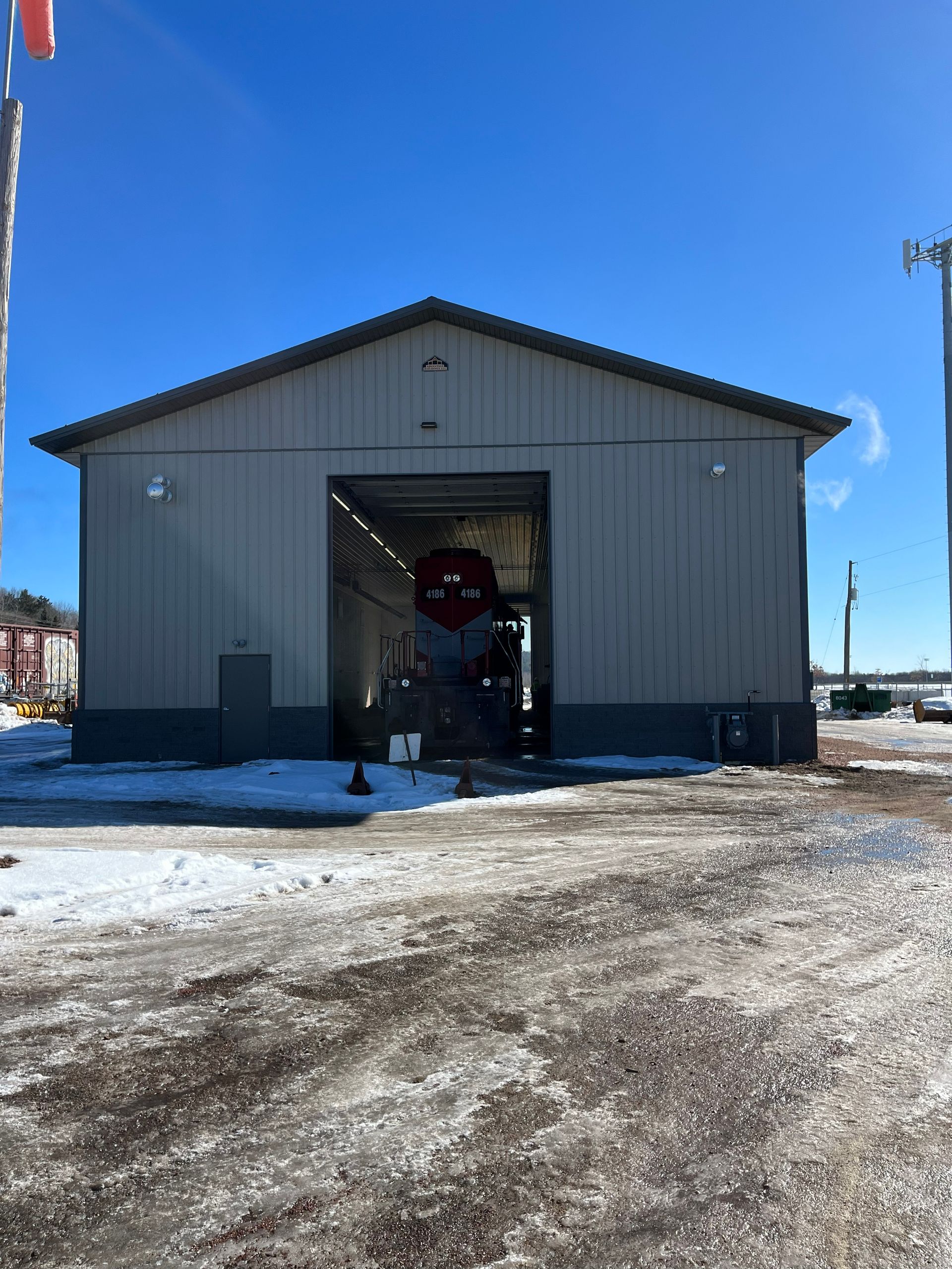 Brown metal garage with two doors on gravel driveway, surrounded by trees.