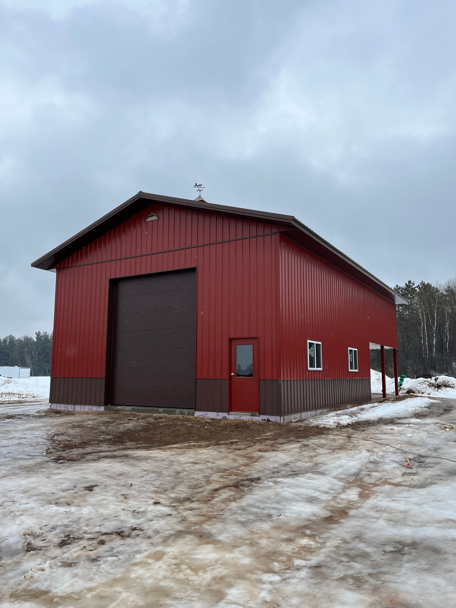 Red metal barn with brown door and trim, set in a snowy landscape.