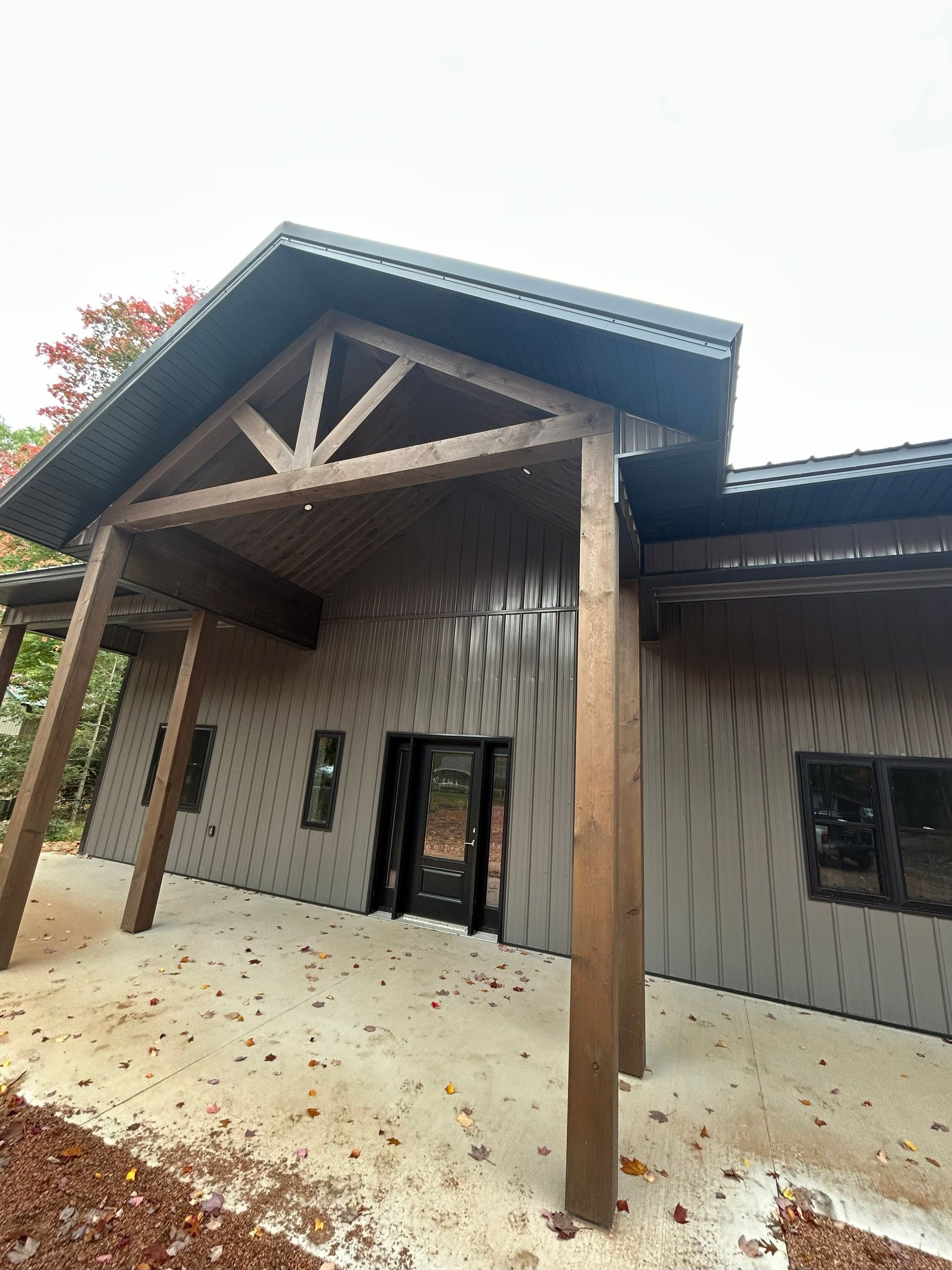 Exterior view of a modern brown house with a covered entryway supported by wooden beams.