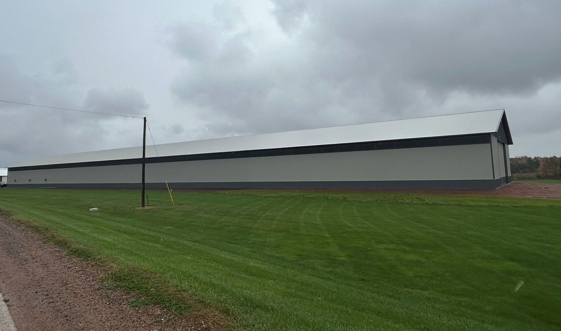 Long, gray building with a dark roof and trim, on a green lawn under a cloudy sky.