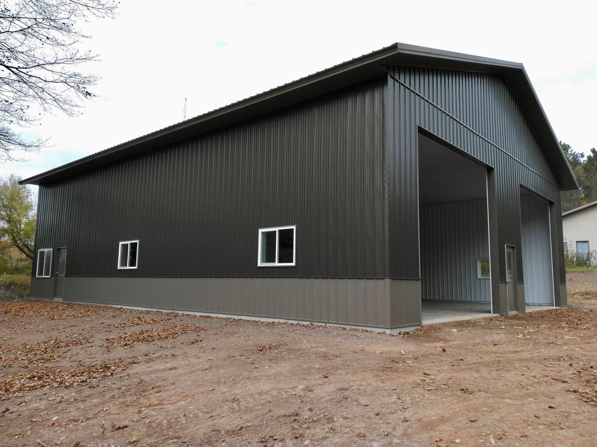Dark grey metal building with large opening, windows, and concrete foundation.
