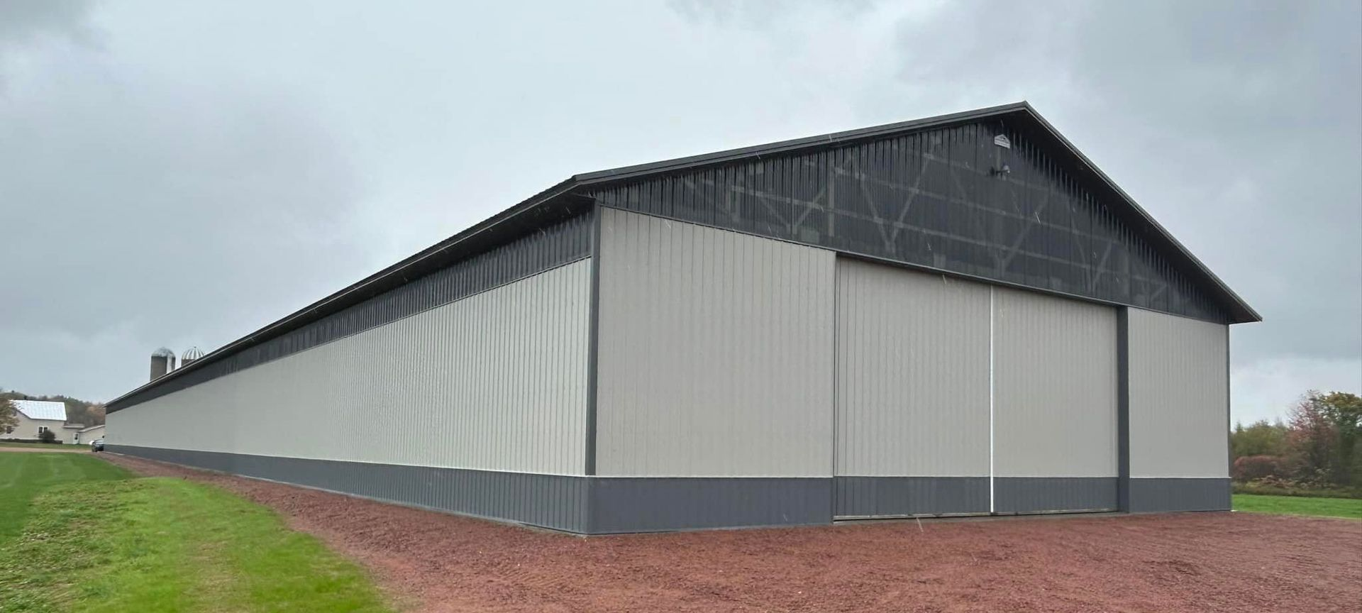 Large agricultural building with gray siding and roof under a cloudy sky.