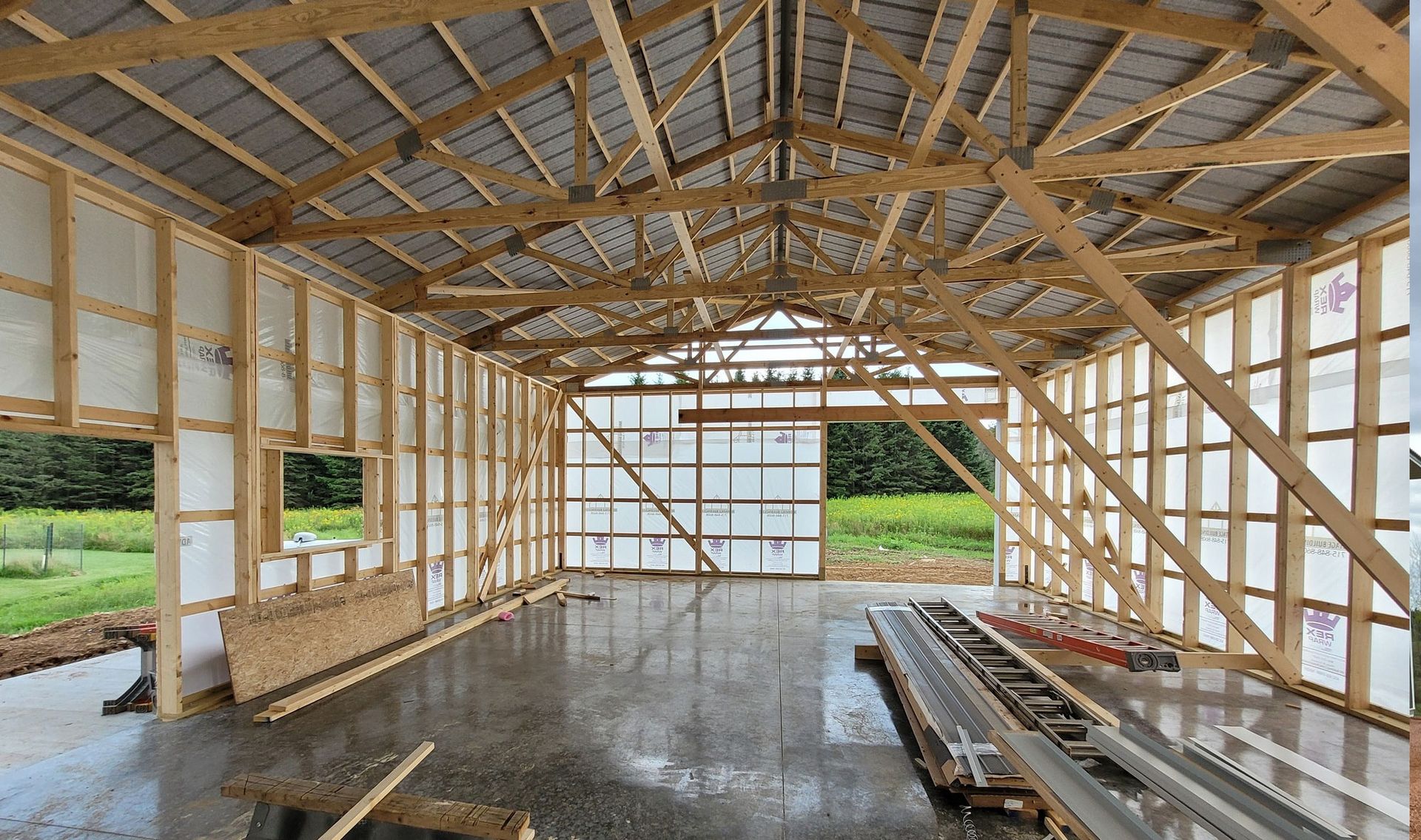 Interior view of a wooden building frame under construction with a concrete floor and a partially built roof.