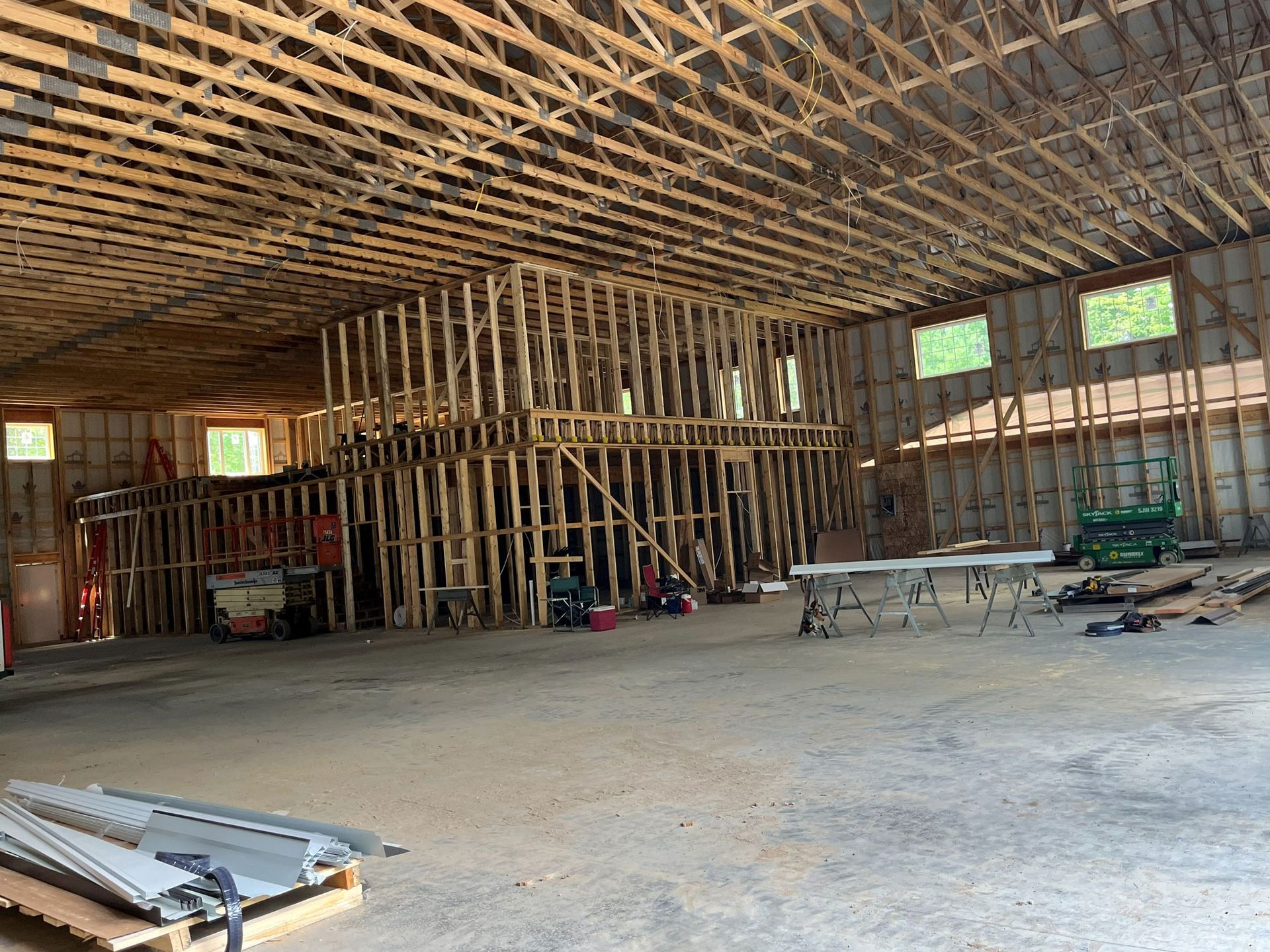 Interior of a large unfinished building with wooden framing, construction materials, and natural light from windows.