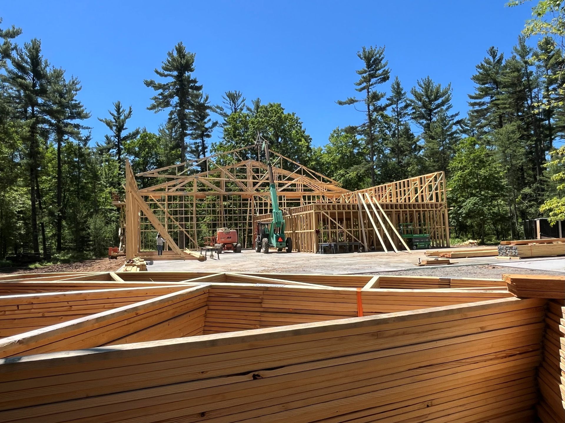 Construction site with wooden framing for a building against a backdrop of trees and blue sky.