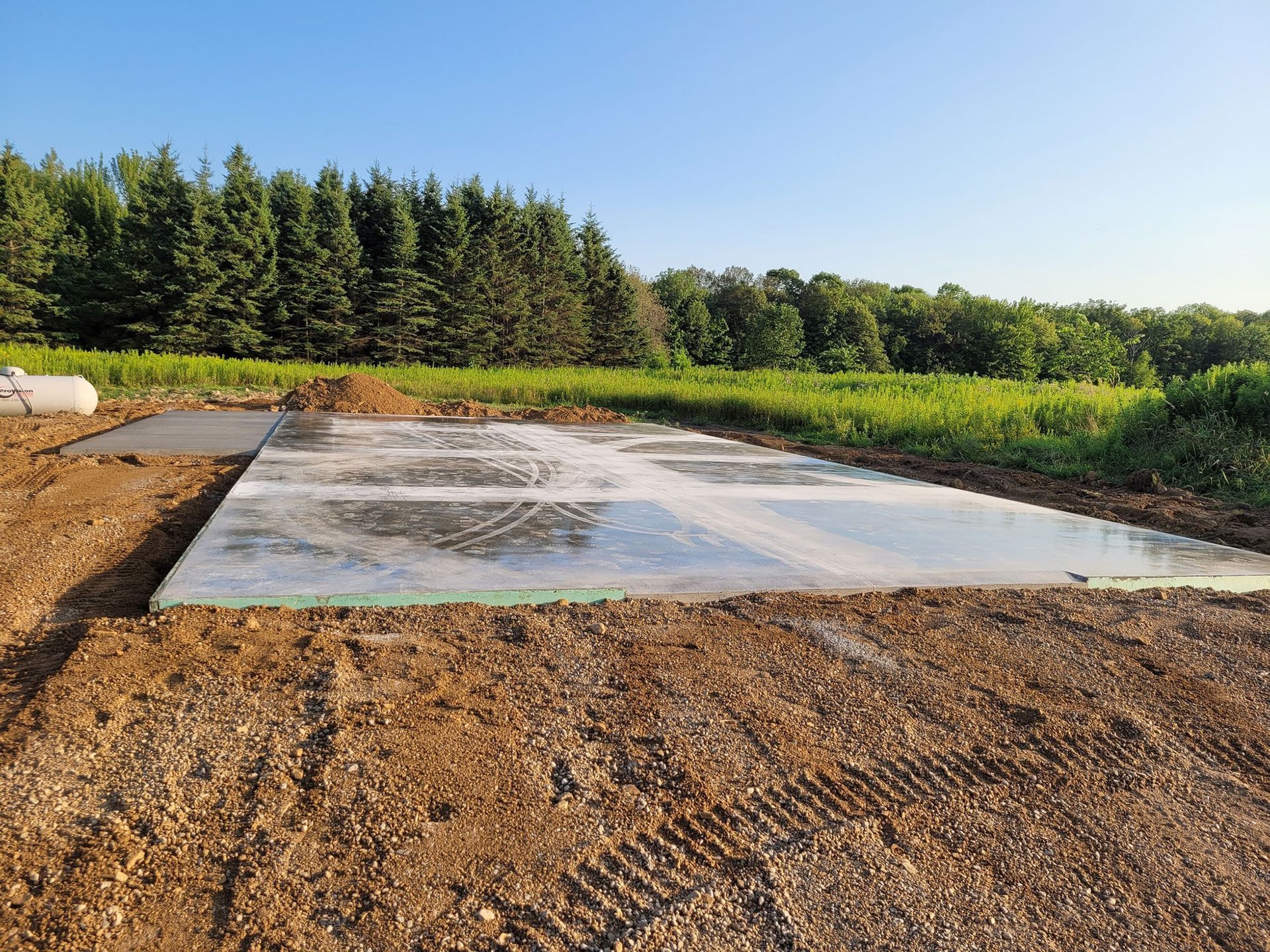 Concrete slab in a dirt clearing, trees in background, clear sky.