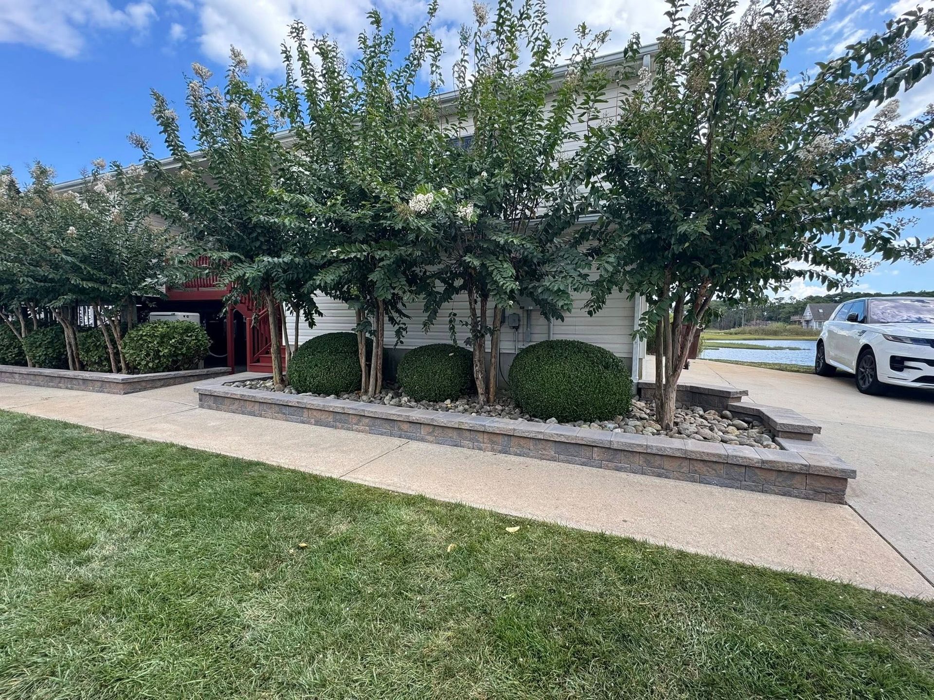 Front of a house with manicured shrubs, a walkway, and a parked white SUV under a blue sky