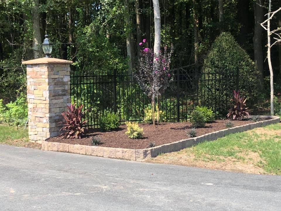 A stone pillar is in the middle of a driveway next to a fence.