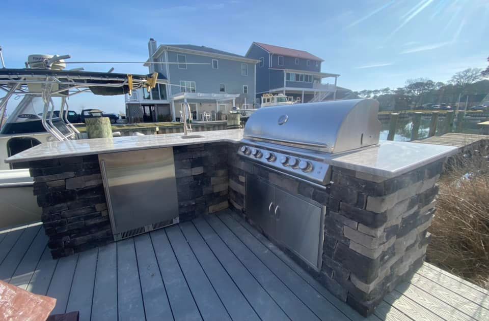 A stainless steel grill is sitting on top of a wooden deck next to a body of water.