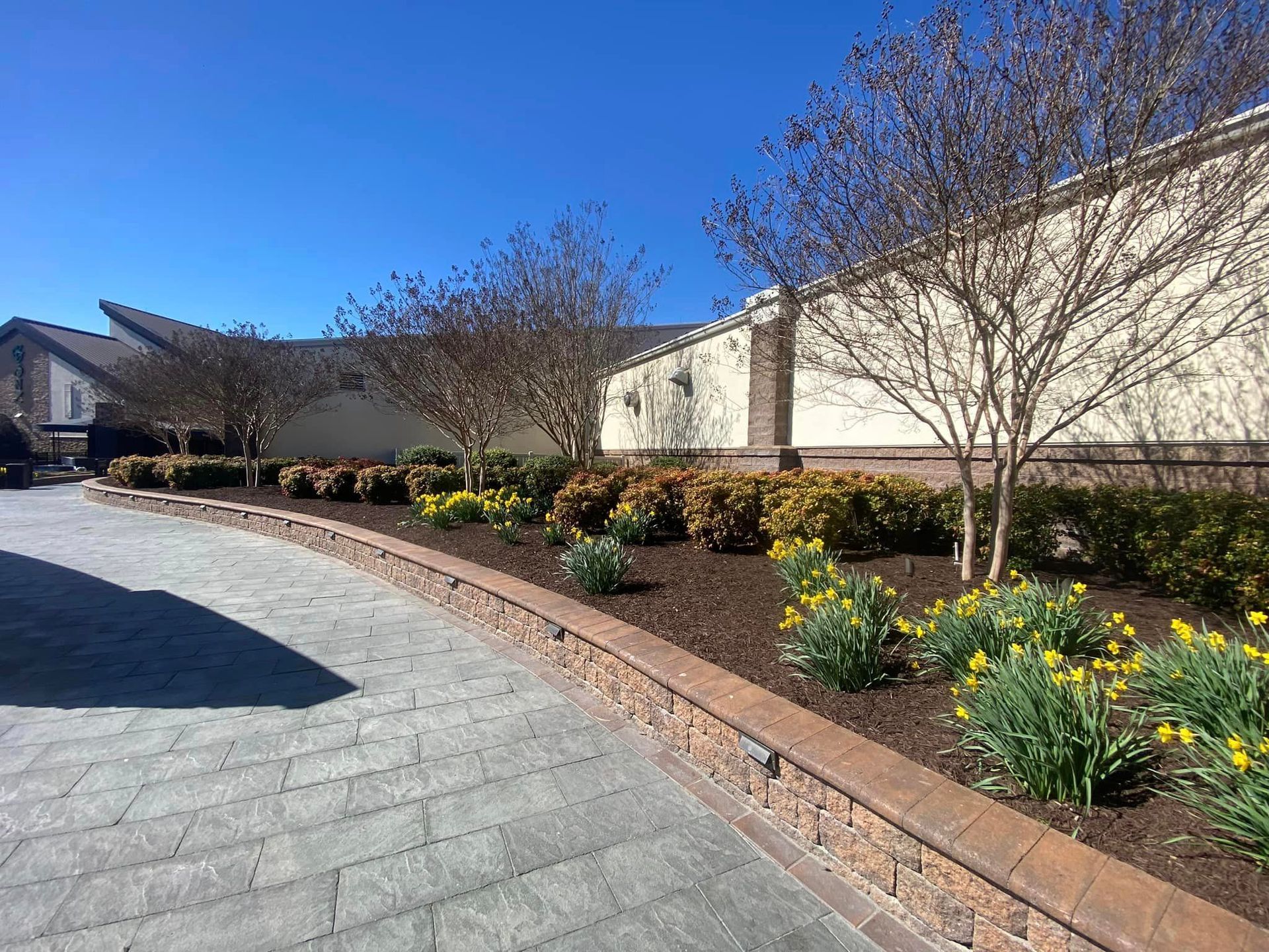 A brick driveway leading to a house with flowers and trees.