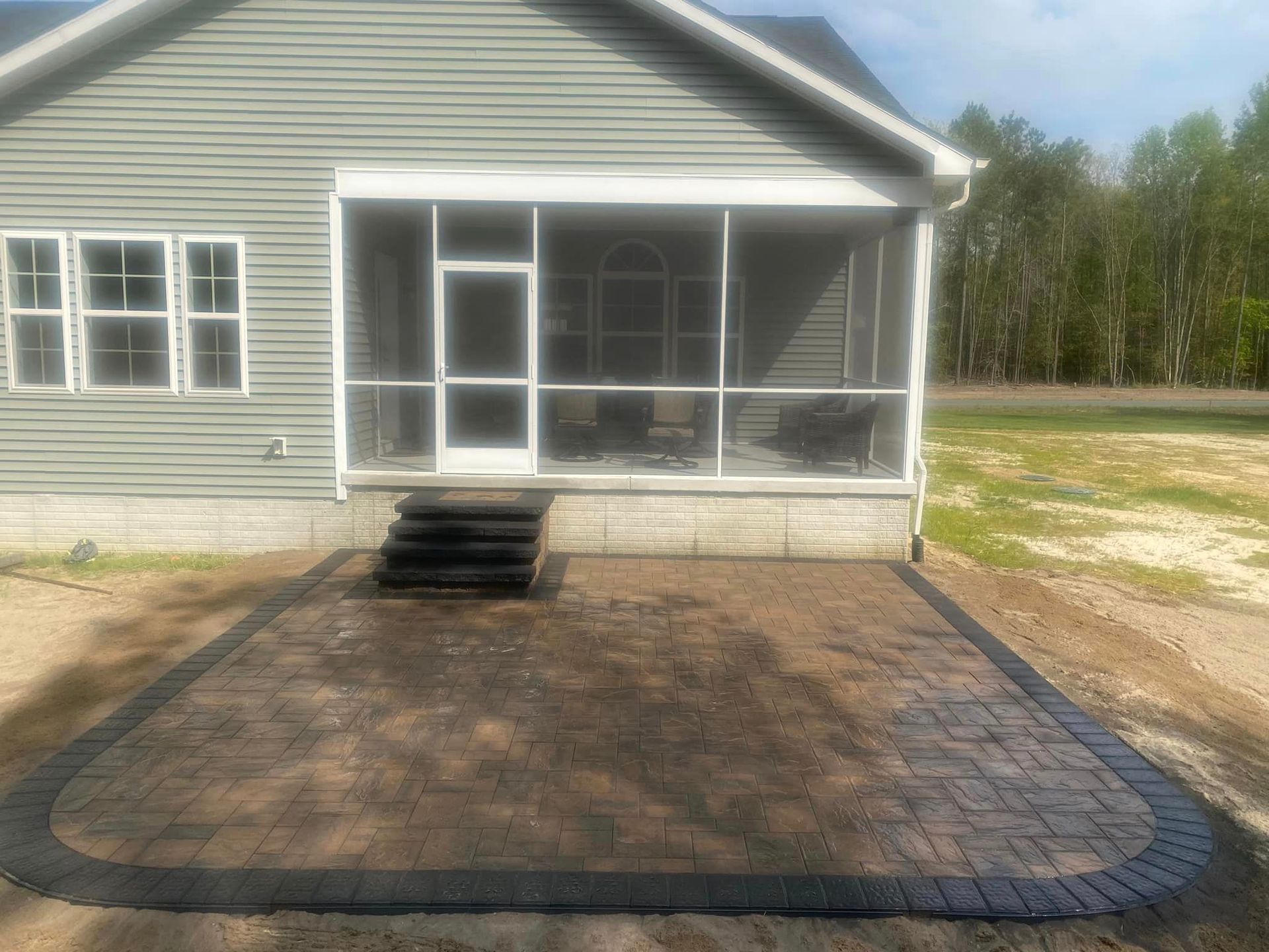 A house with a screened in porch and a patio in front of it.
