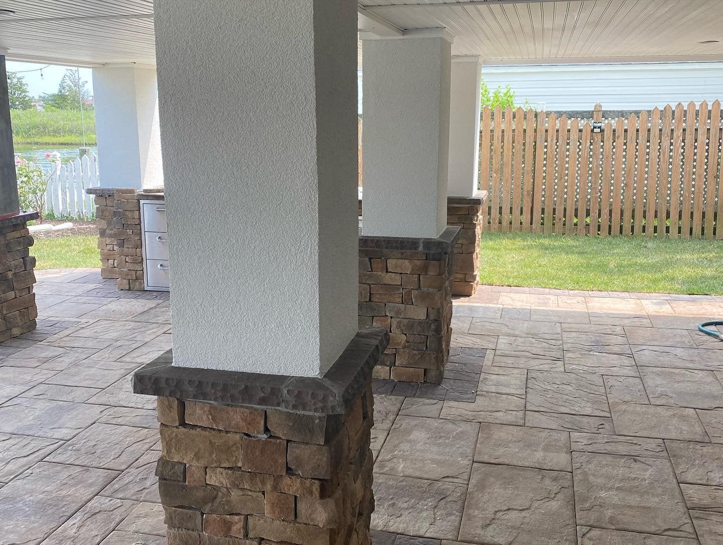 A patio with columns and a wooden fence in the background.