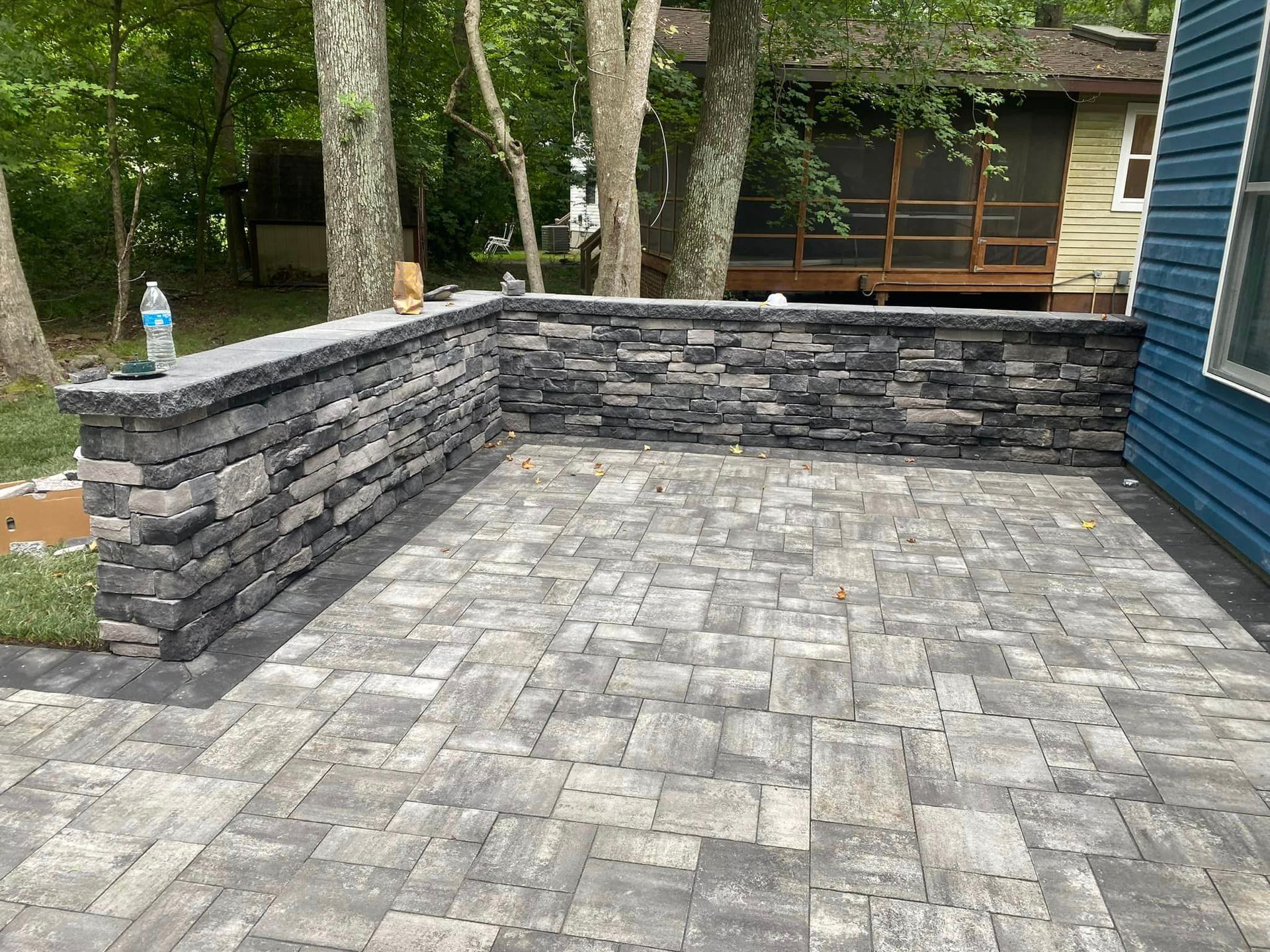 A patio with a stone wall and a screened in porch in the background.