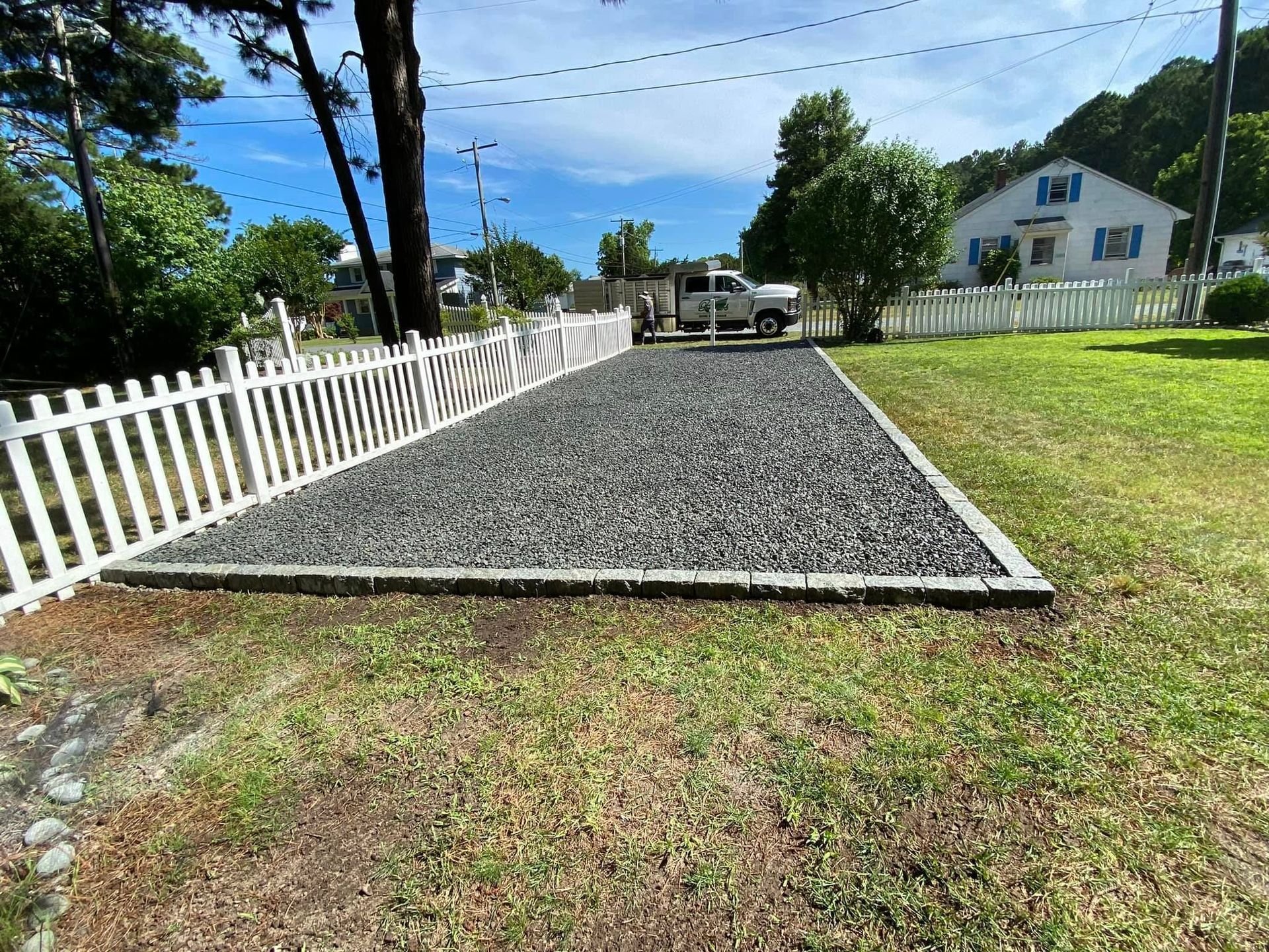 A gravel driveway with a white picket fence in front of a house.