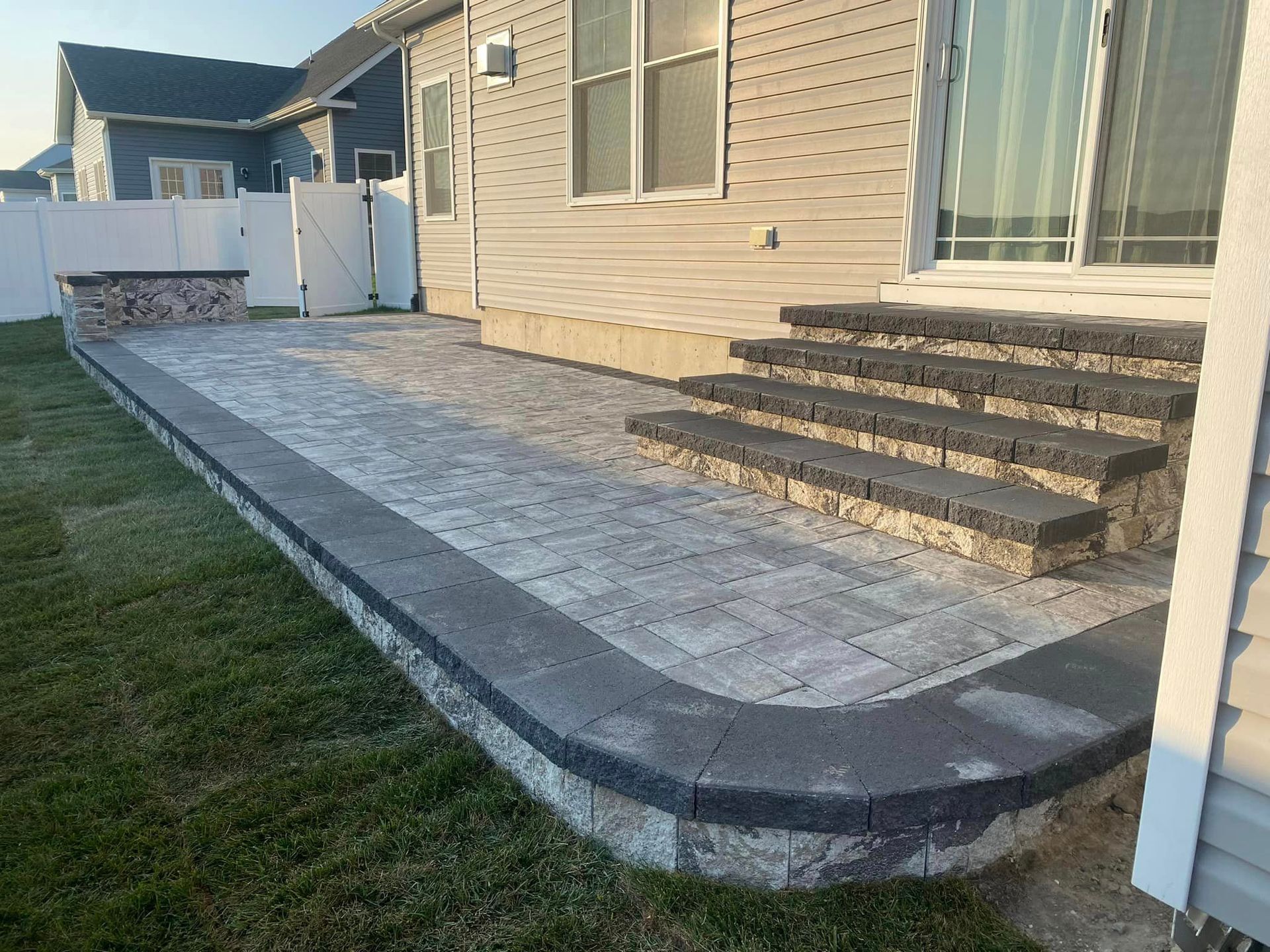Brick patio with steps and a low wall, next to a house, on grass.