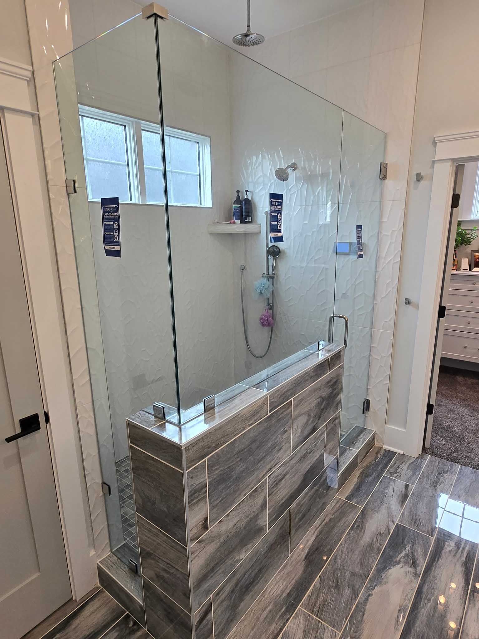 A modern bathroom shower featuring a glass enclosure with a low, wood-look tiled wall and grey wood-patterned floor tiles.