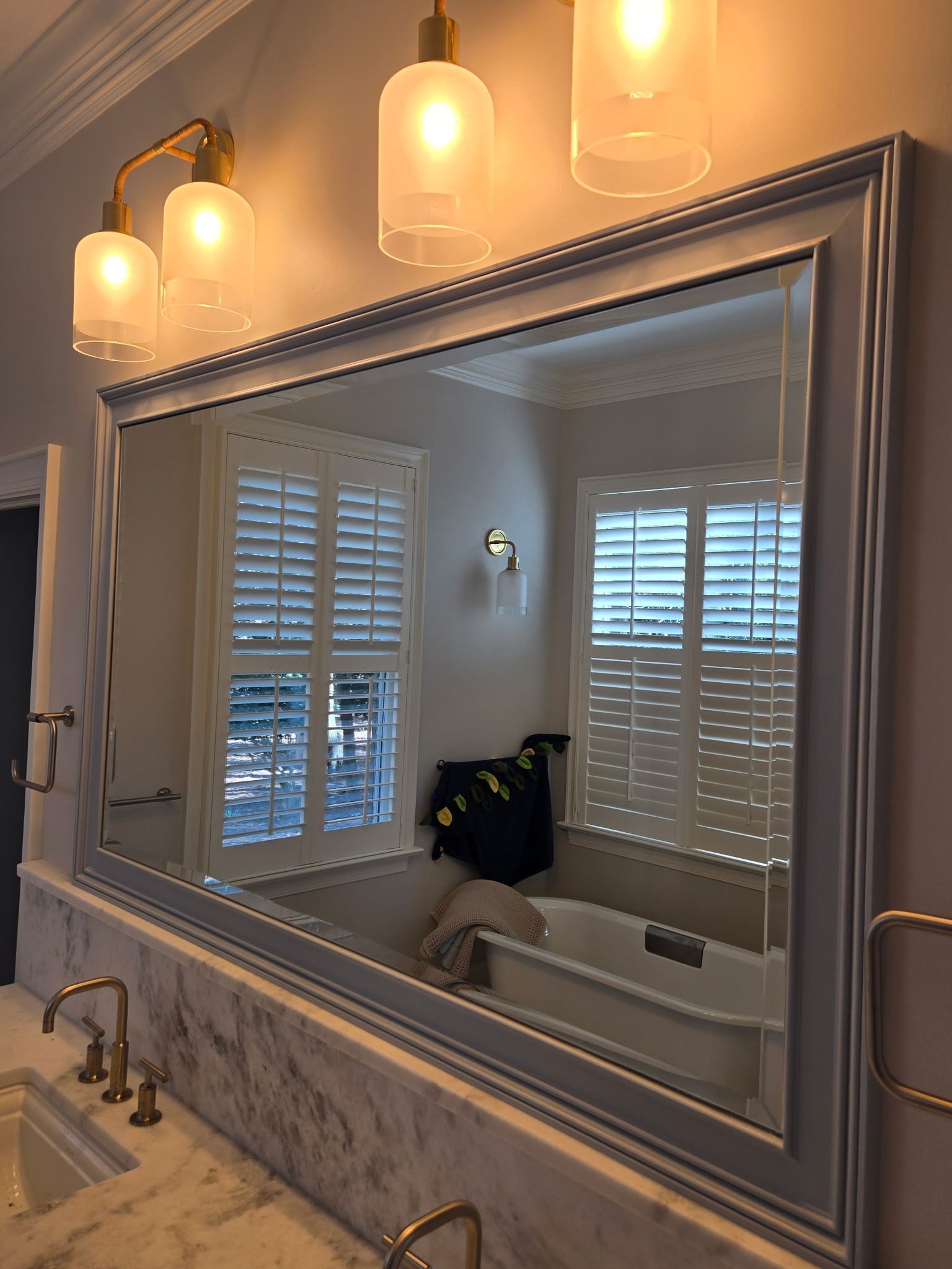 A bathroom vanity mirror with a grey frame, illuminated by two hanging glass pendant lights above a marble countertop.