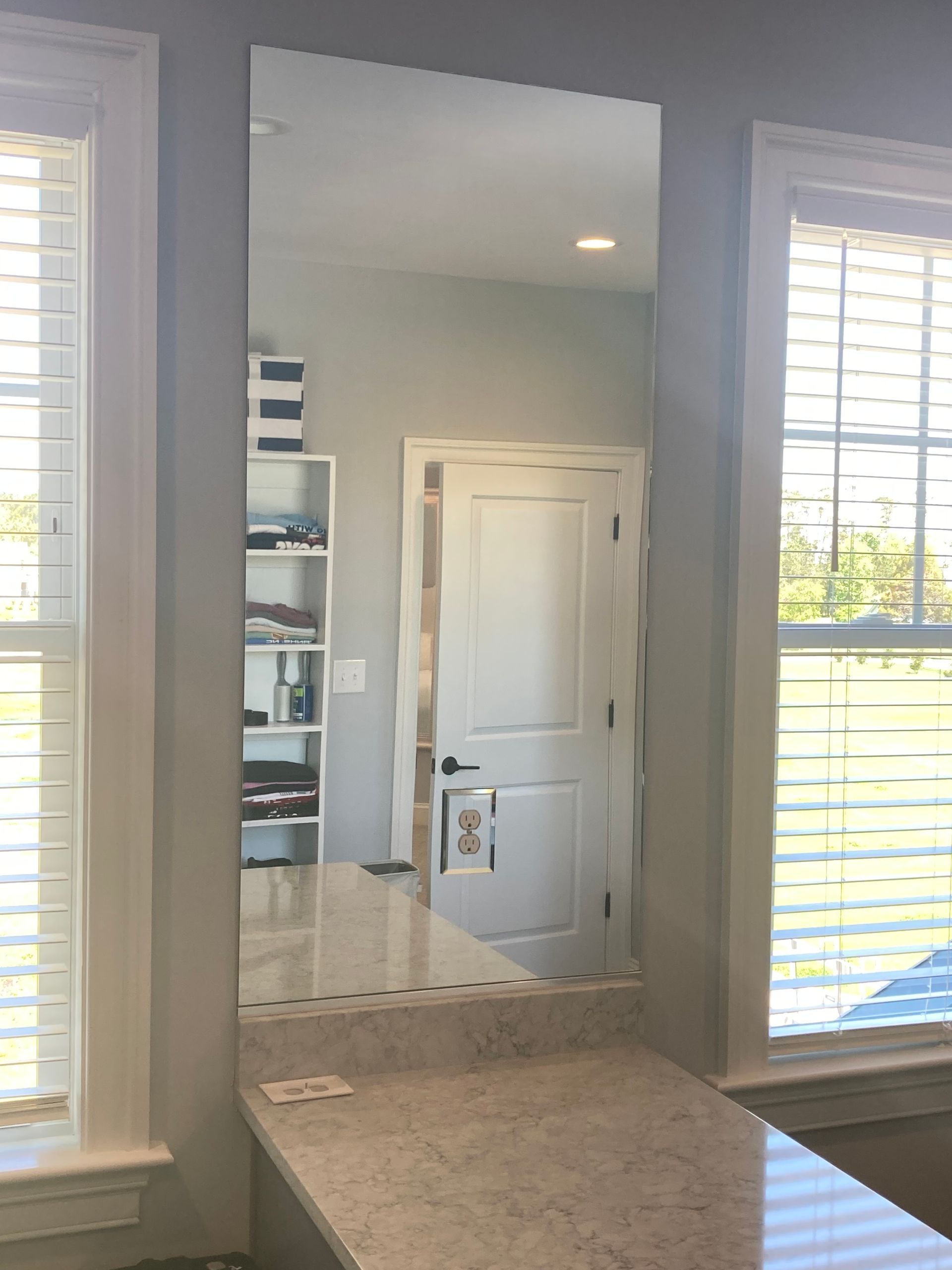 A rectangular wall mirror centered between two windows above a light-colored granite countertop.