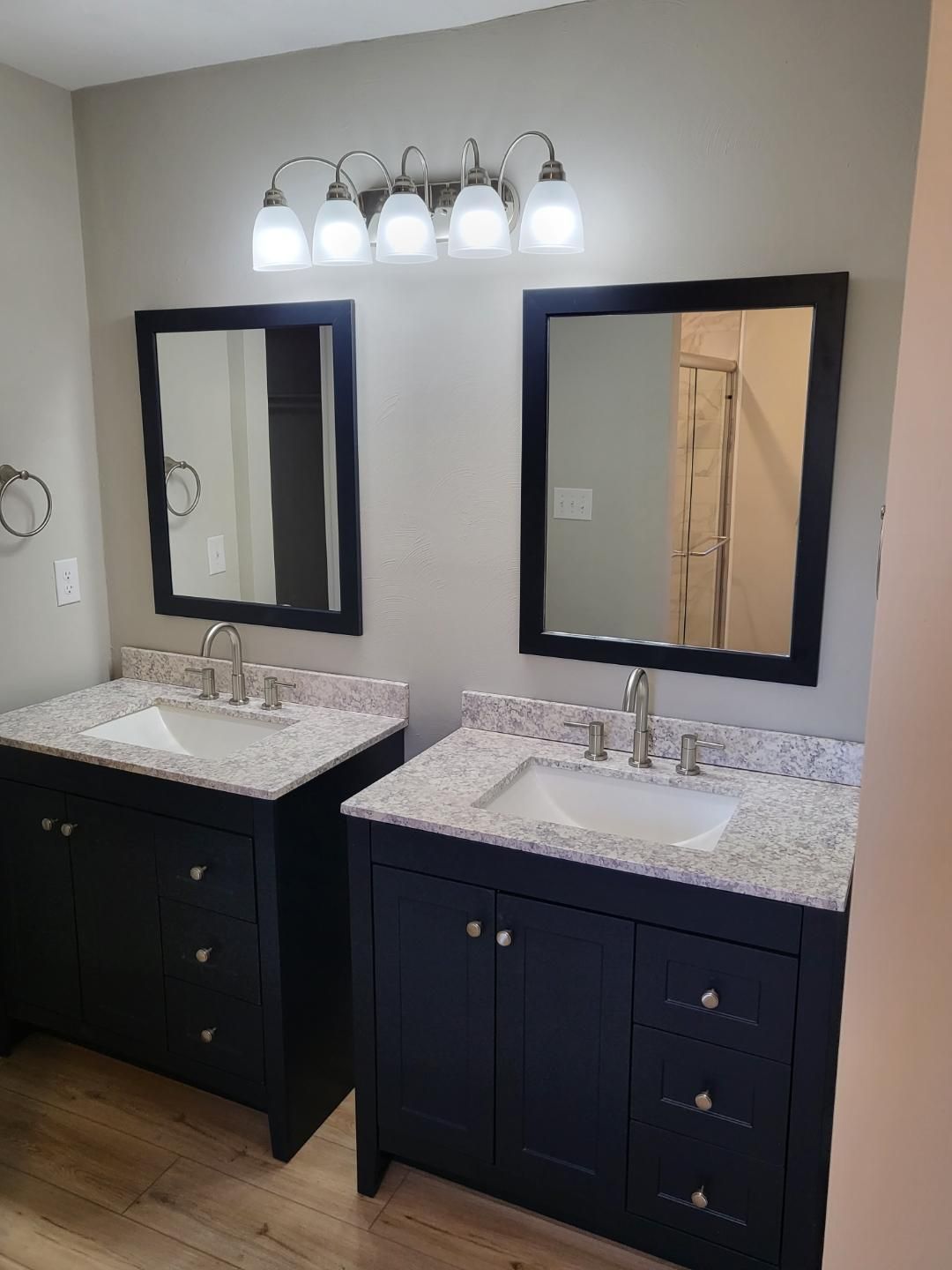 Double vanity with dark cabinets, speckled granite countertops, two mirrors, and a four-bulb light fixture in a bathroom.