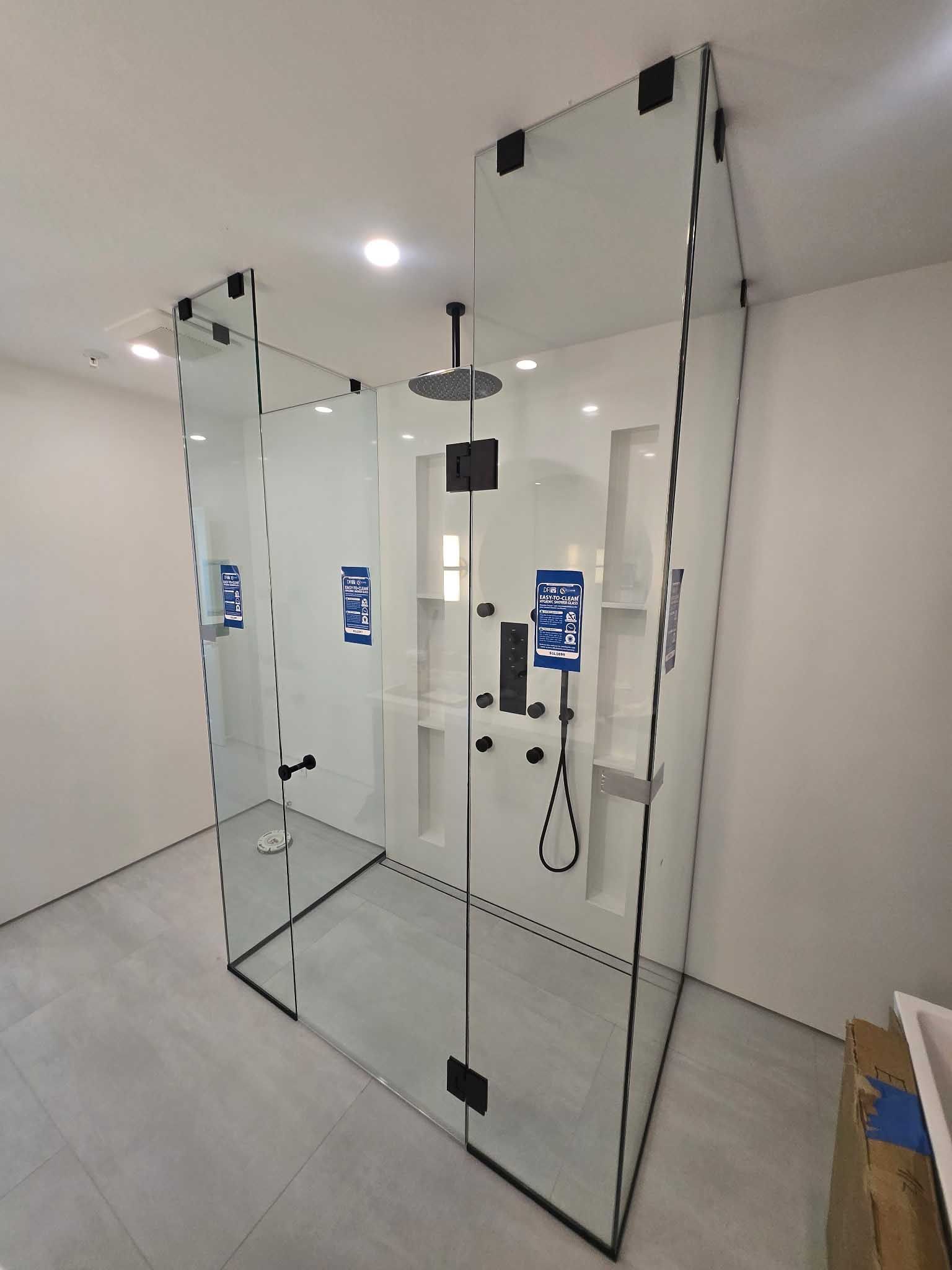 A walk-in shower with clear glass panels, black hardware, and a rain showerhead, set against white tiled walls.