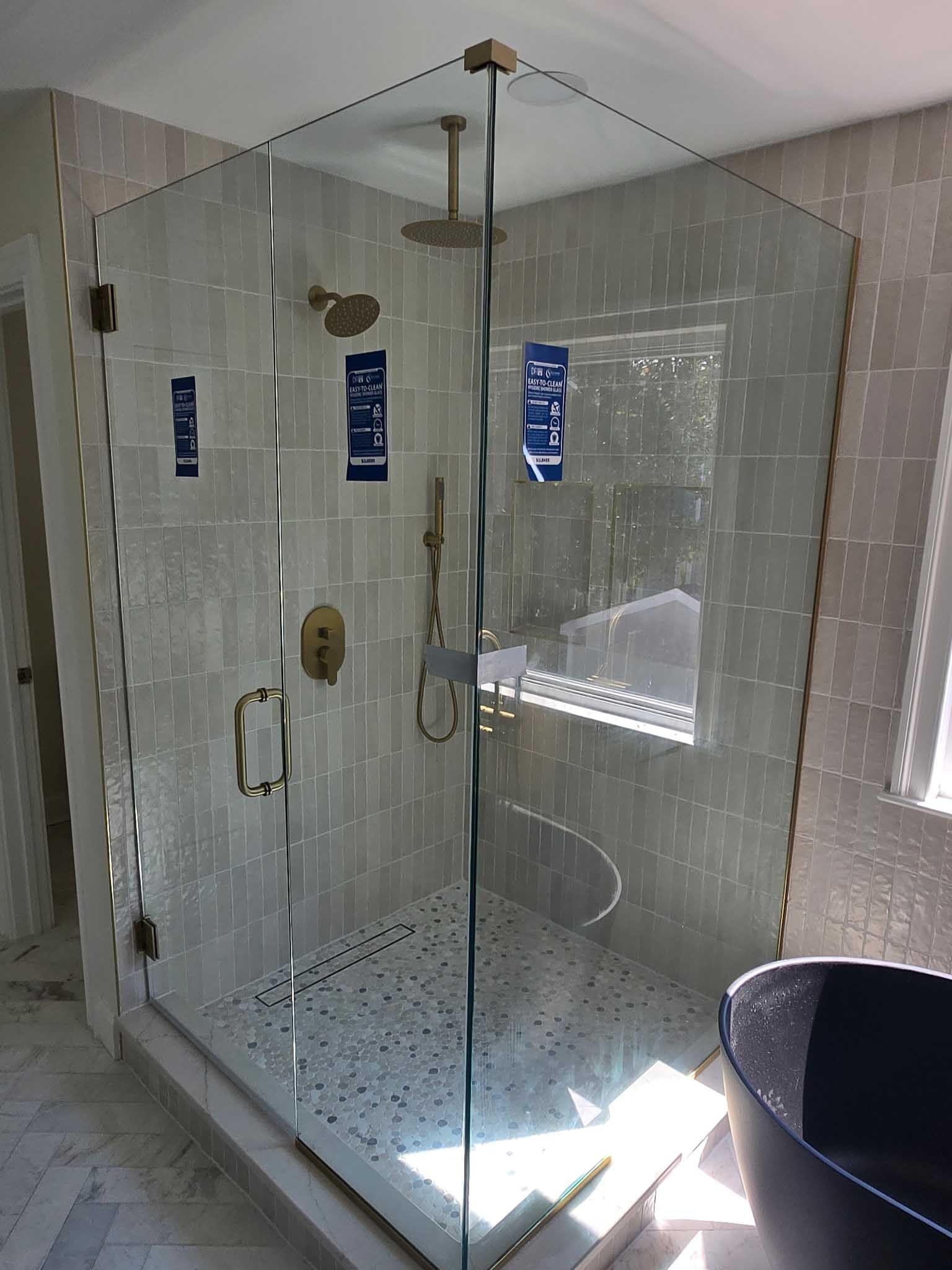A glass walk-in shower with gold fixtures and a patterned tile floor in a tiled bathroom.