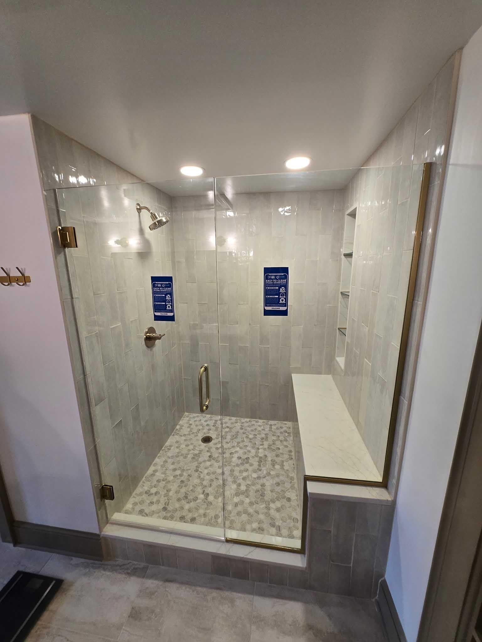 A modern walk-in shower with light marble tile walls, a pebble-stone floor, a glass door, and a built-in bench.