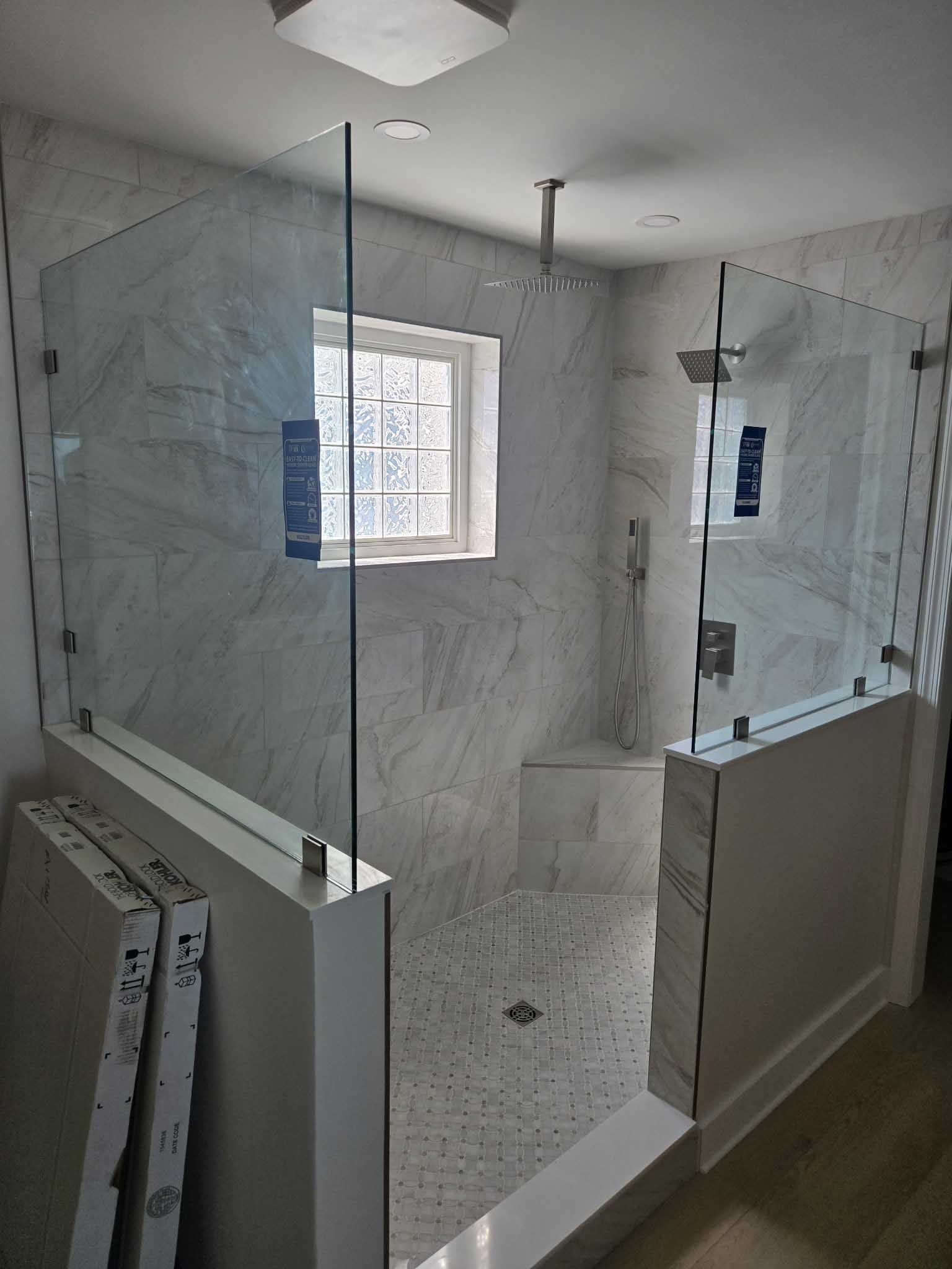 A modern walk-in shower with white marble-patterned tile, glass partitions, a built-in bench, and a rain-style showerhead.