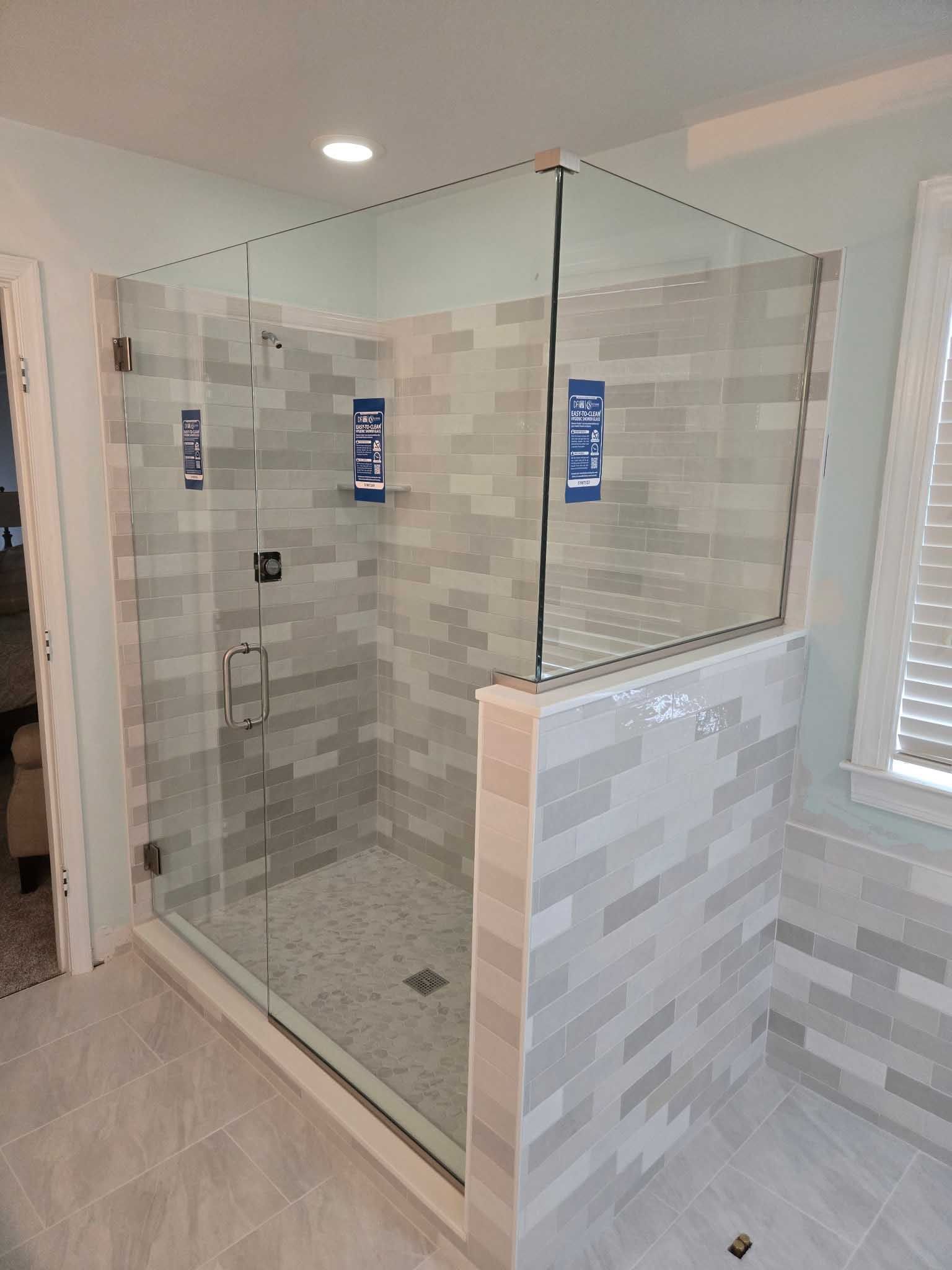 A walk-in shower with a glass door and partial tiled wall in a room with light grey floor and wall tiles.
