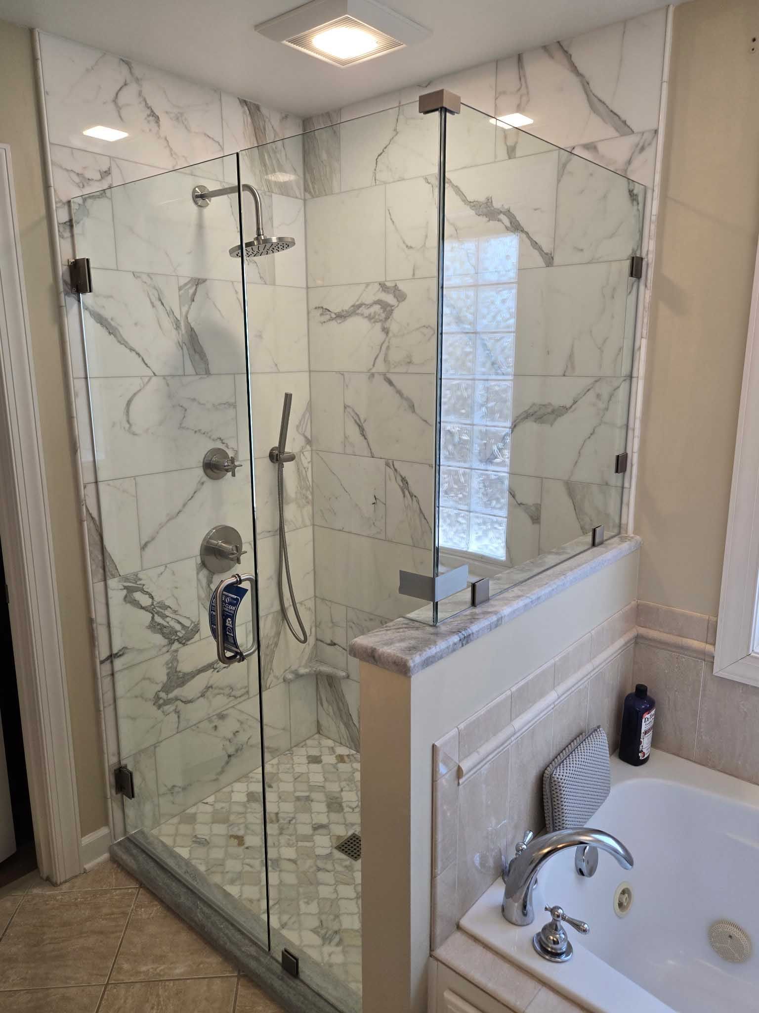 A glass-enclosed shower with white marble-patterned tiles, a rainfall showerhead, and a adjacent white soaking tub.