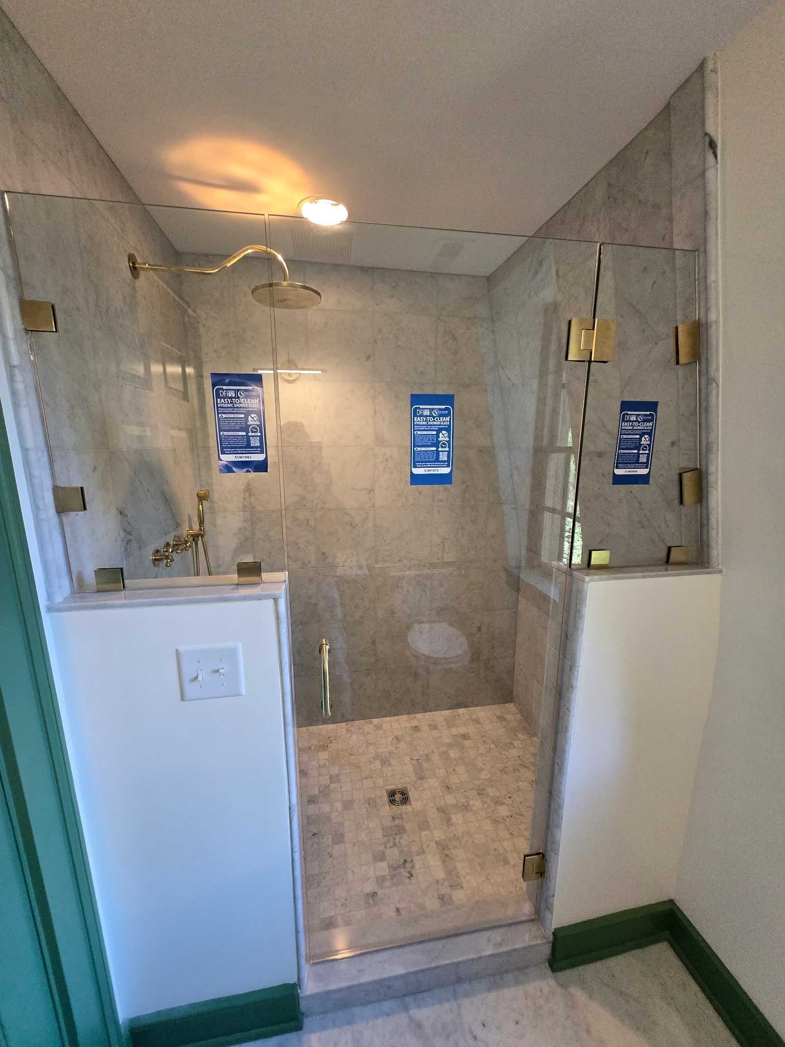 A walk-in shower with gold hardware, a stone-tiled floor, and glass panels mounted on two short white pony walls.