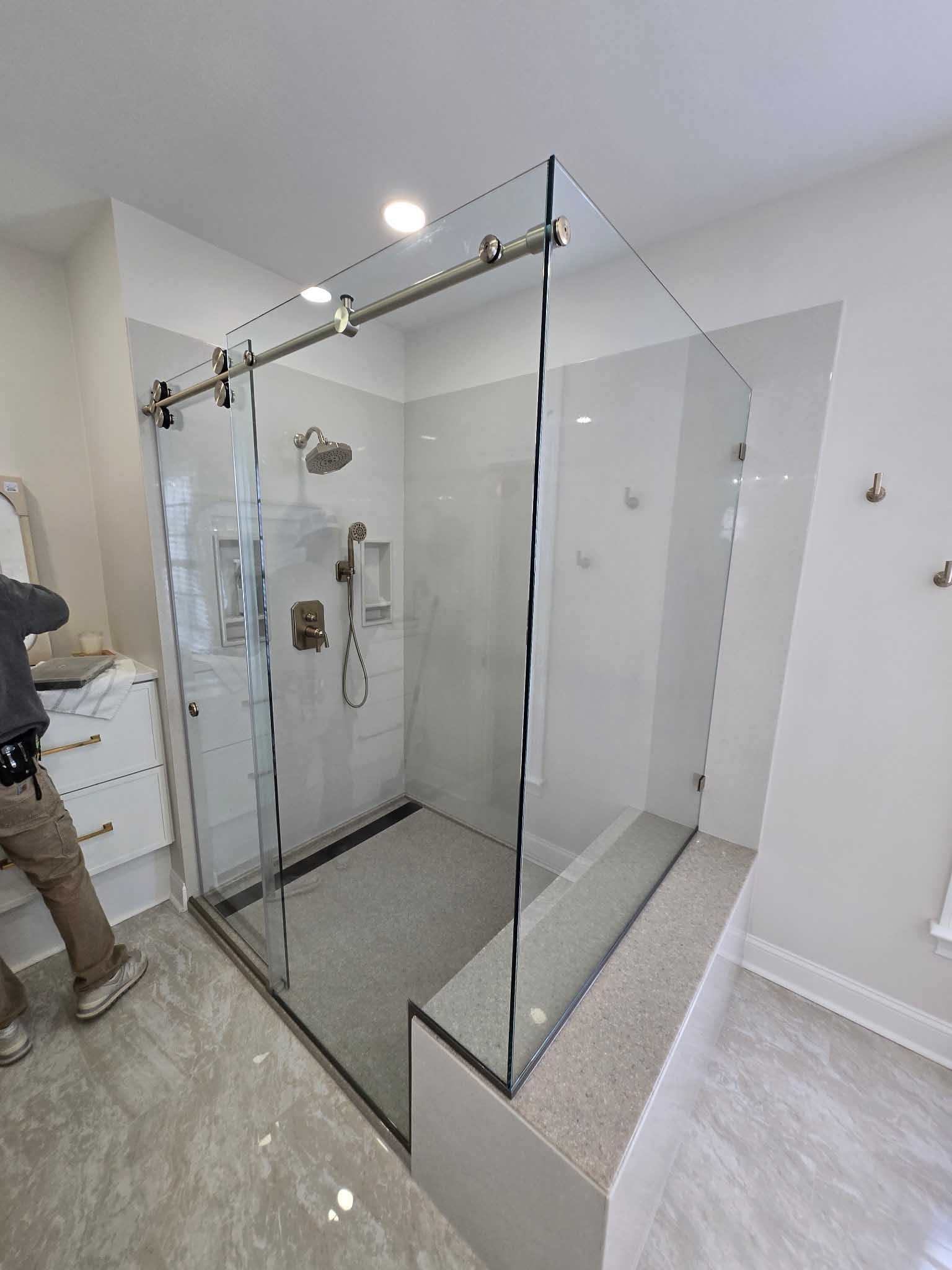 A modern bathroom featuring a frameless glass shower enclosure with a sliding door, a stone bench, and chrome hardware.
