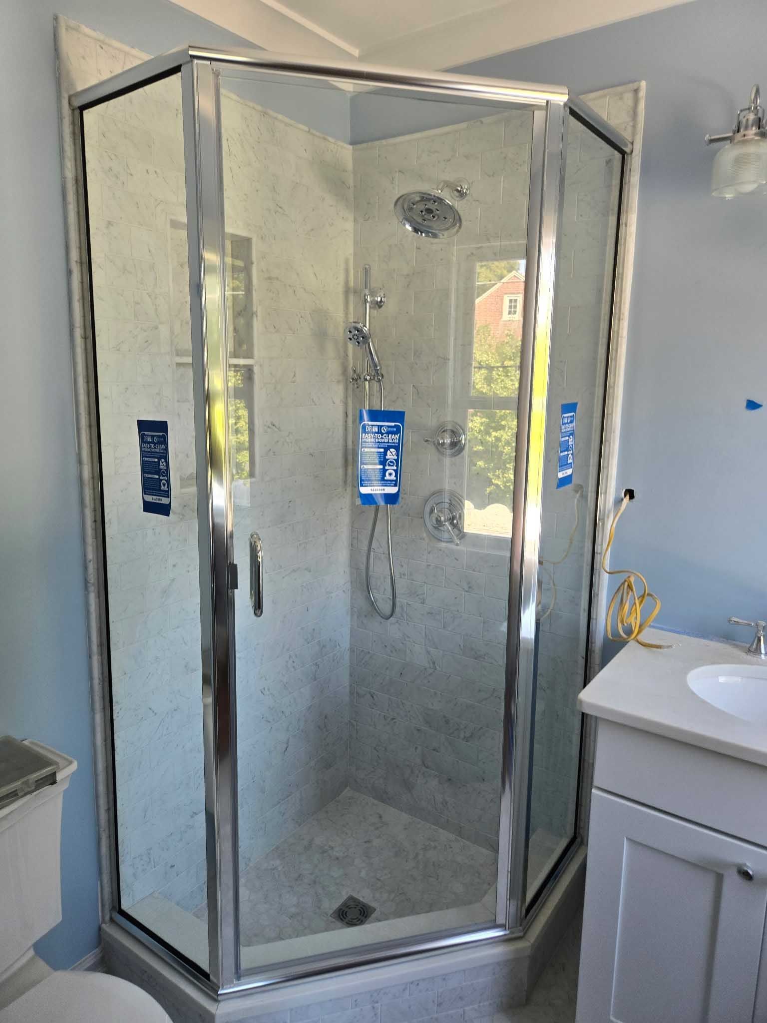 A corner neo-angle glass shower enclosure with chrome trim in a bathroom with light blue walls.