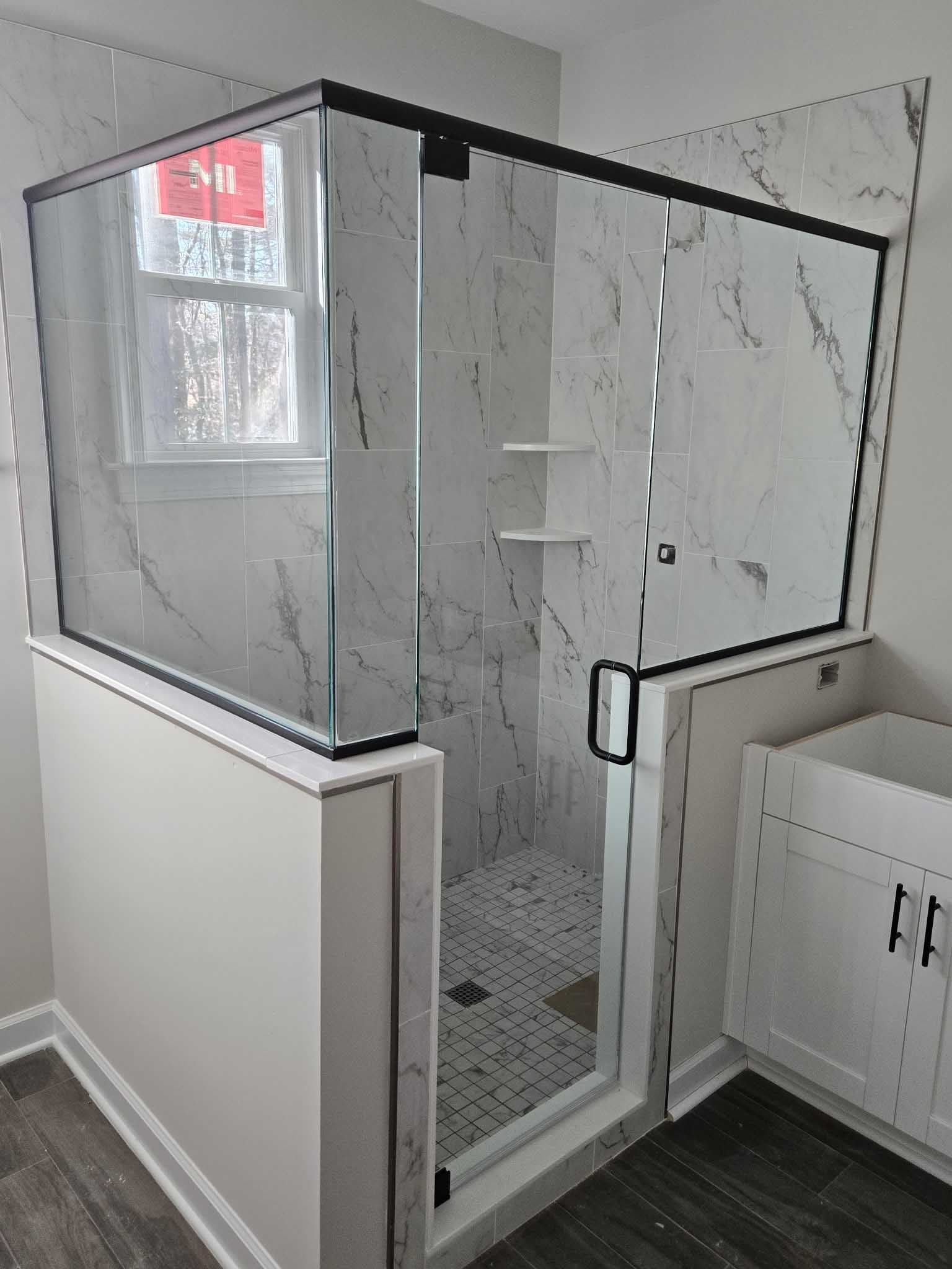 A modern walk-in shower with black hardware, marble-patterned walls, and a glass enclosure in a bathroom.