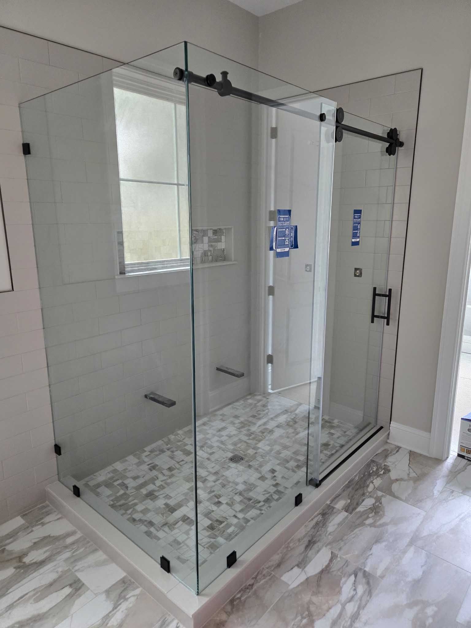 A modern, glass-enclosed shower stall with a sliding glass door, black hardware, and tiled walls and floor.