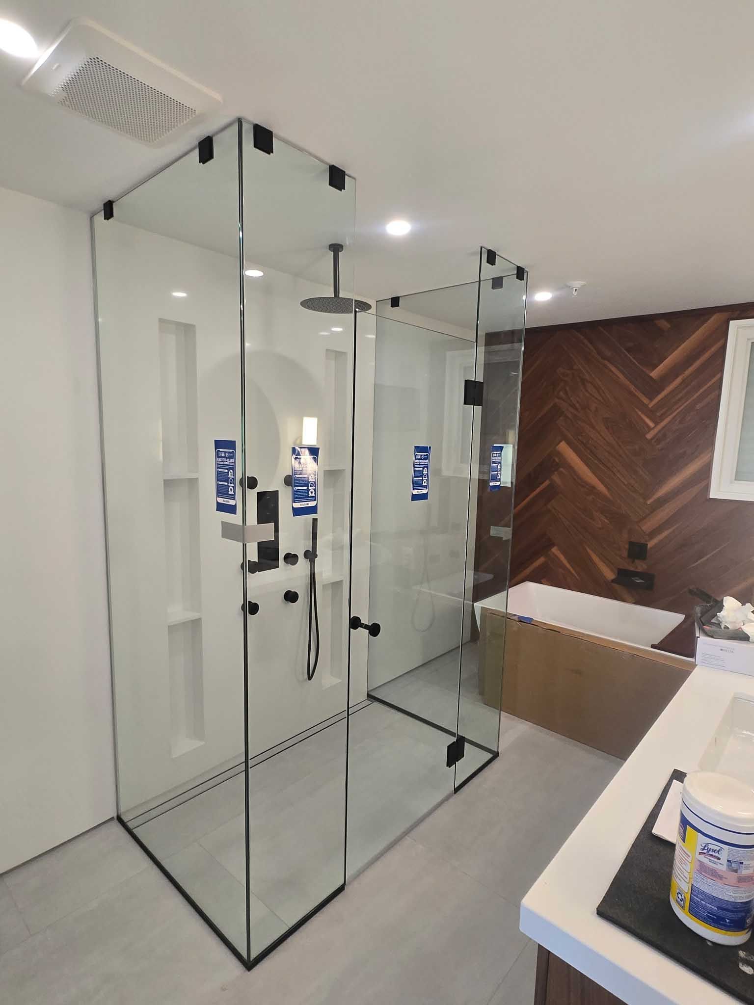 Modern bathroom with a clear glass shower enclosure, black hardware, white recessed shelving, and dark wood herringbone wall.