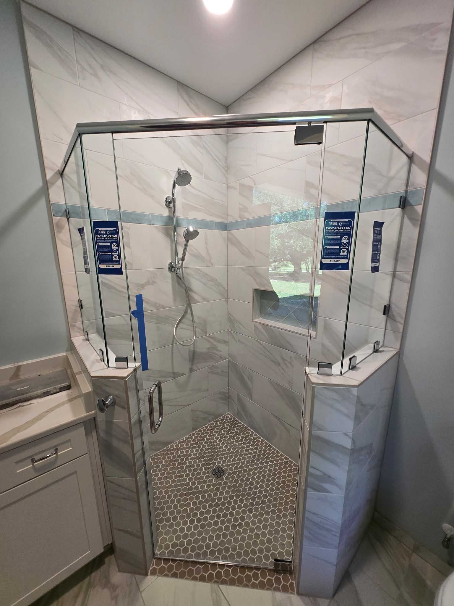 Corner shower stall with glass doors, marble-patterned tile walls, and a pebble-style floor, situated in a bathroom.