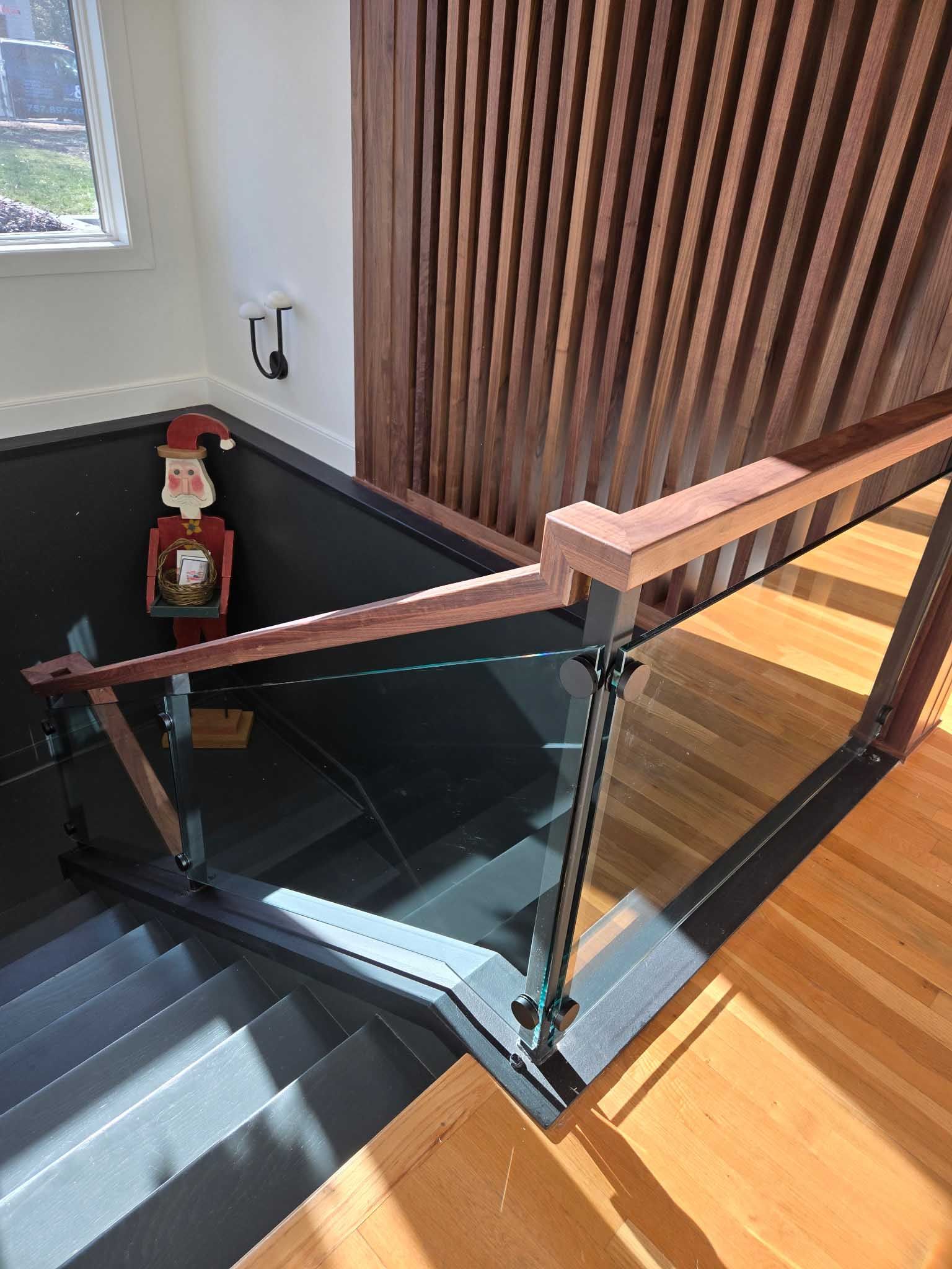 A modern wooden and glass staircase railing overlooks a dark-painted staircase with a decorative nutcracker figure.