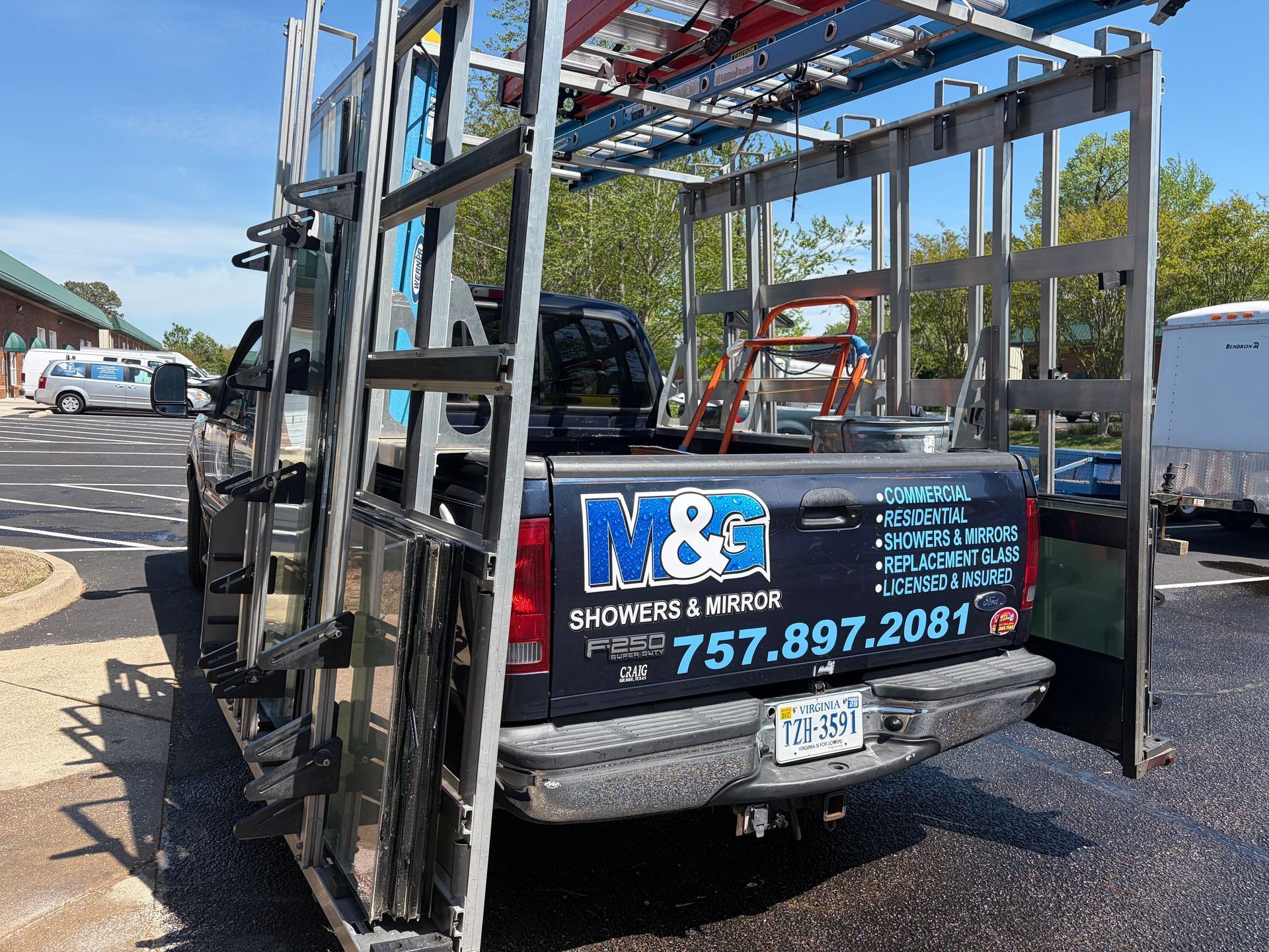 Two blue utility trucks facing each other on a roadside, with flatbed trailers and water in the background
