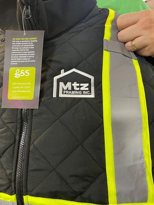 Close-up of a black quilted safety vest with neon yellow reflective stripes and an MTZ logo.