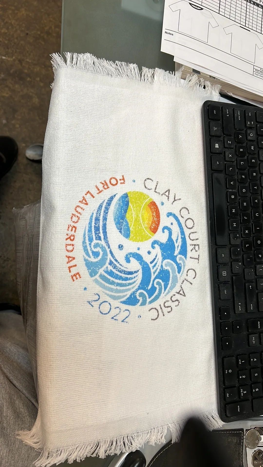 White towel with a colorful circular logo beside a black keyboard on a desk.